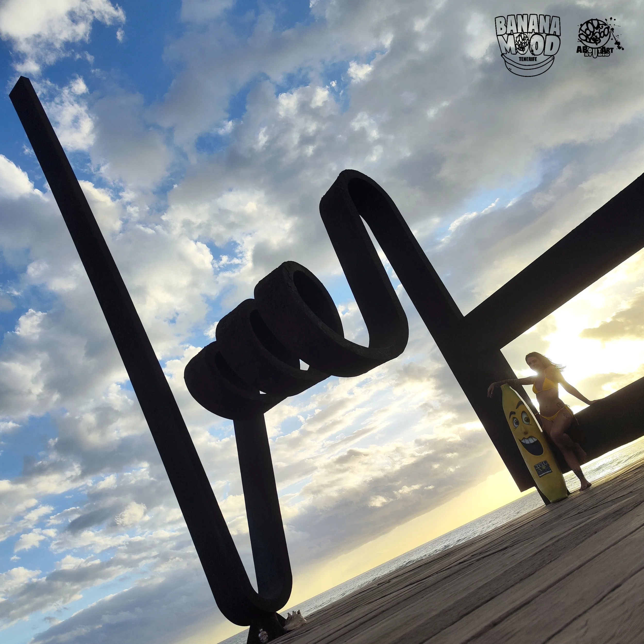 Estructura de metal en forma de letras que dice 'LOVE', con una mujer en traje de baño y una tabla de surf con una expresión feliz, en una playa al atardecer, con cielo nublado y el mar de fondo.