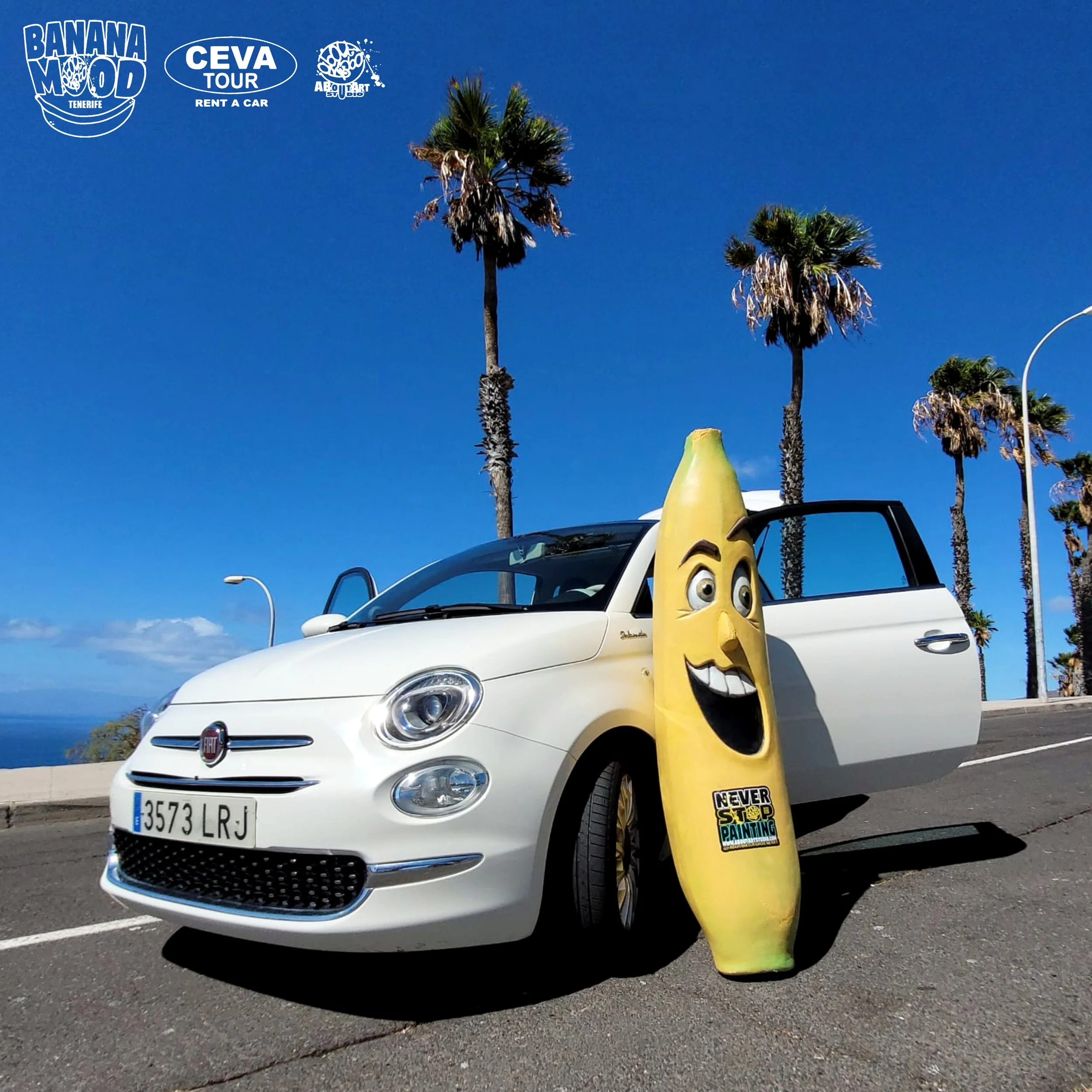 Coche blanco en la carretera con una banana inflable con cara sonriente y etiqueta que dice 'Never Stop Painting', en un fondo de clima soleado y palmeras.