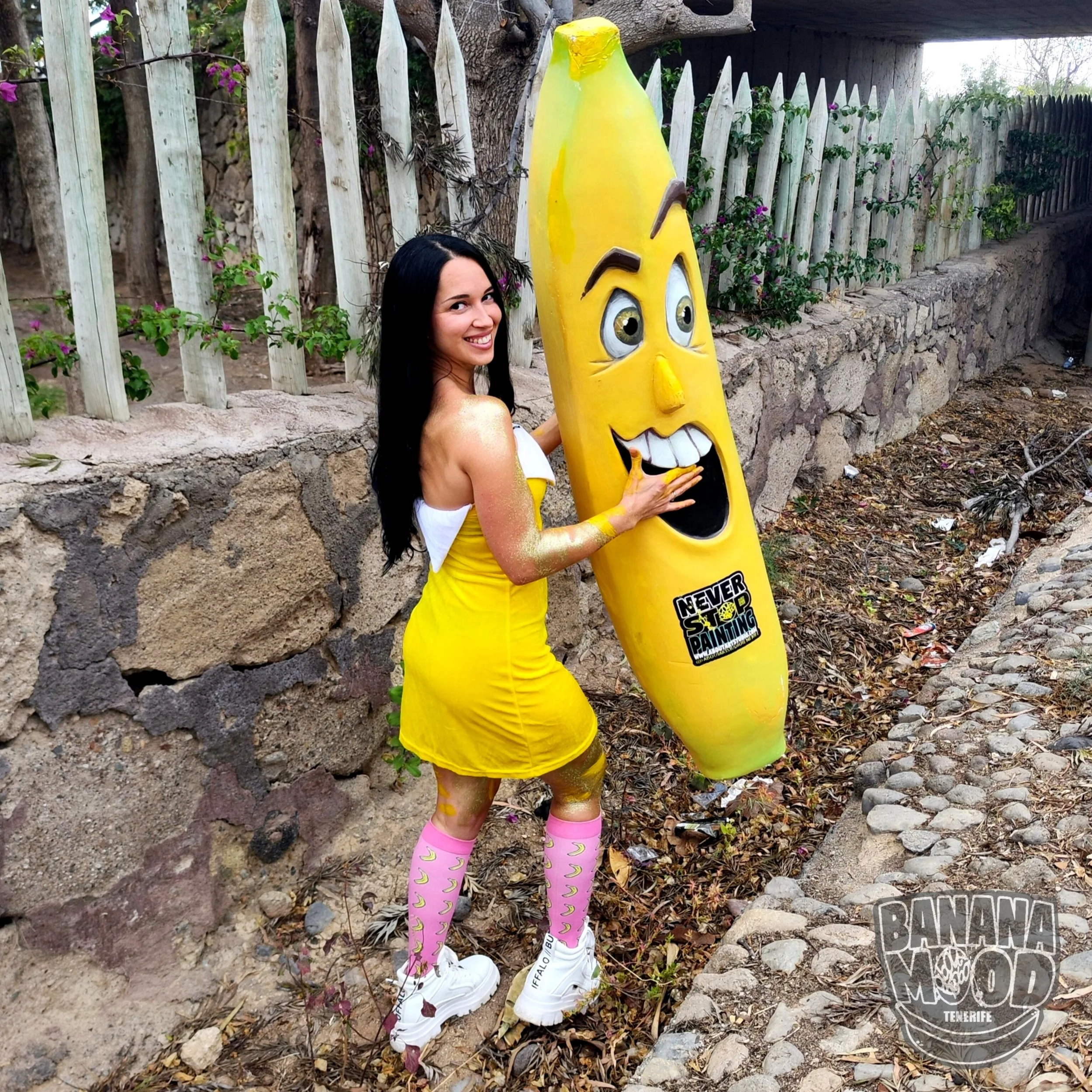 Mujer disfrazada de banana interactuando con una estatua de banana con rostro y expresión divertida en la calle.