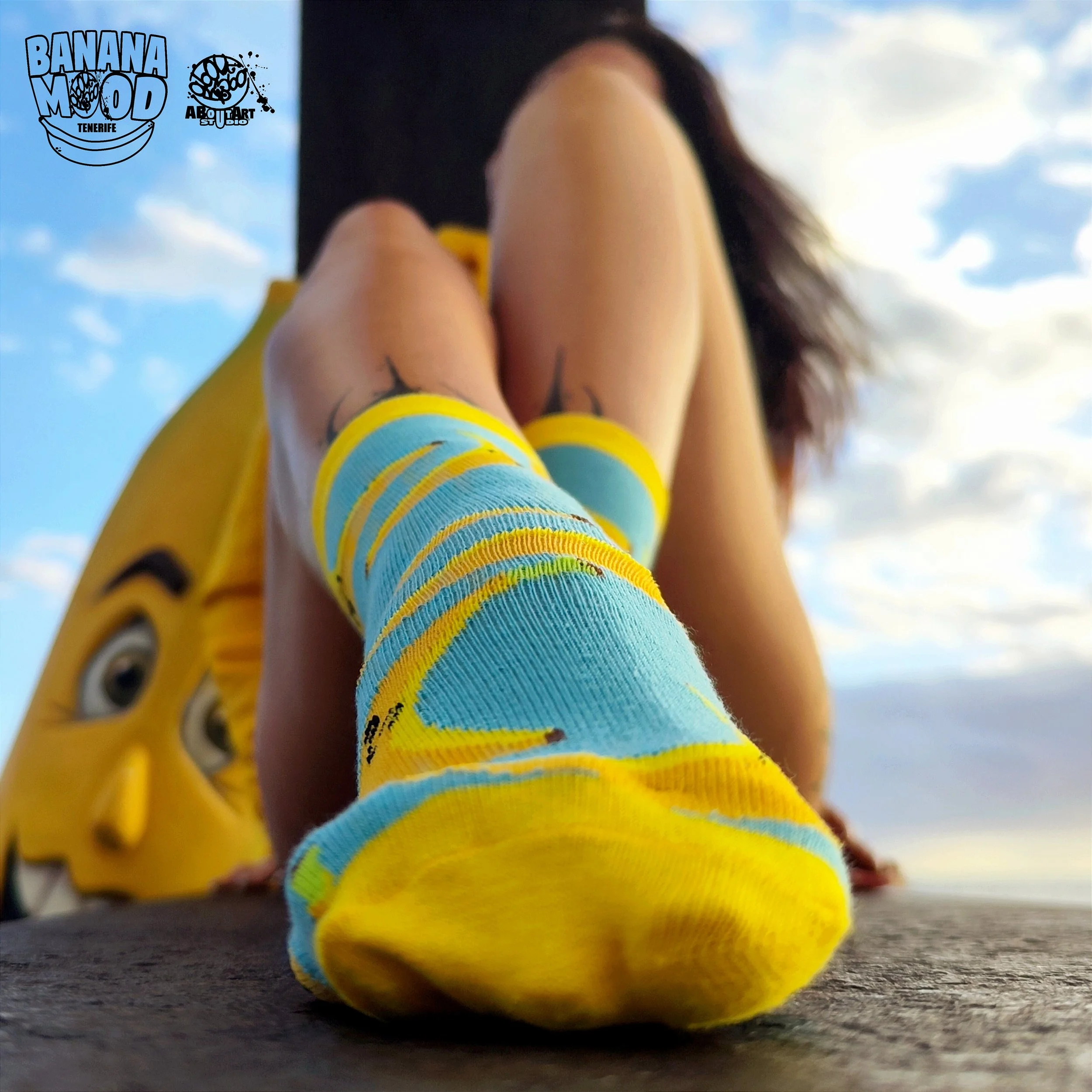 Persona con calcetines color azul y amarillo, en primer plano, en un lugar al aire libre con cielo y nubes, sosteniendo una máscara de la película 'La Máscara' de Jim Carrey.