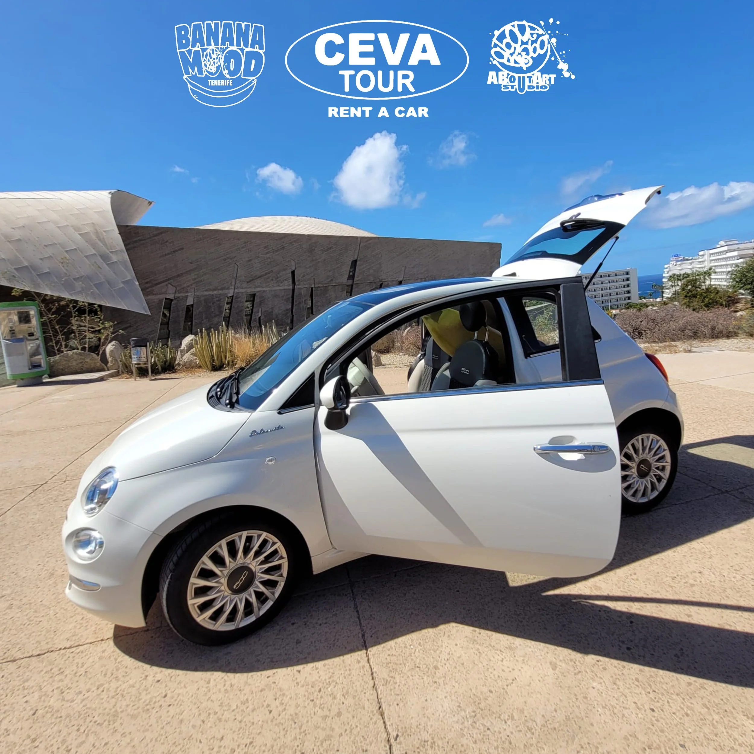 Coche compacto blanco con maletero abierto en un paisaje soleado con arquitectura moderna y cactus en el fondo, bajo un cielo azul con algunas nubes.