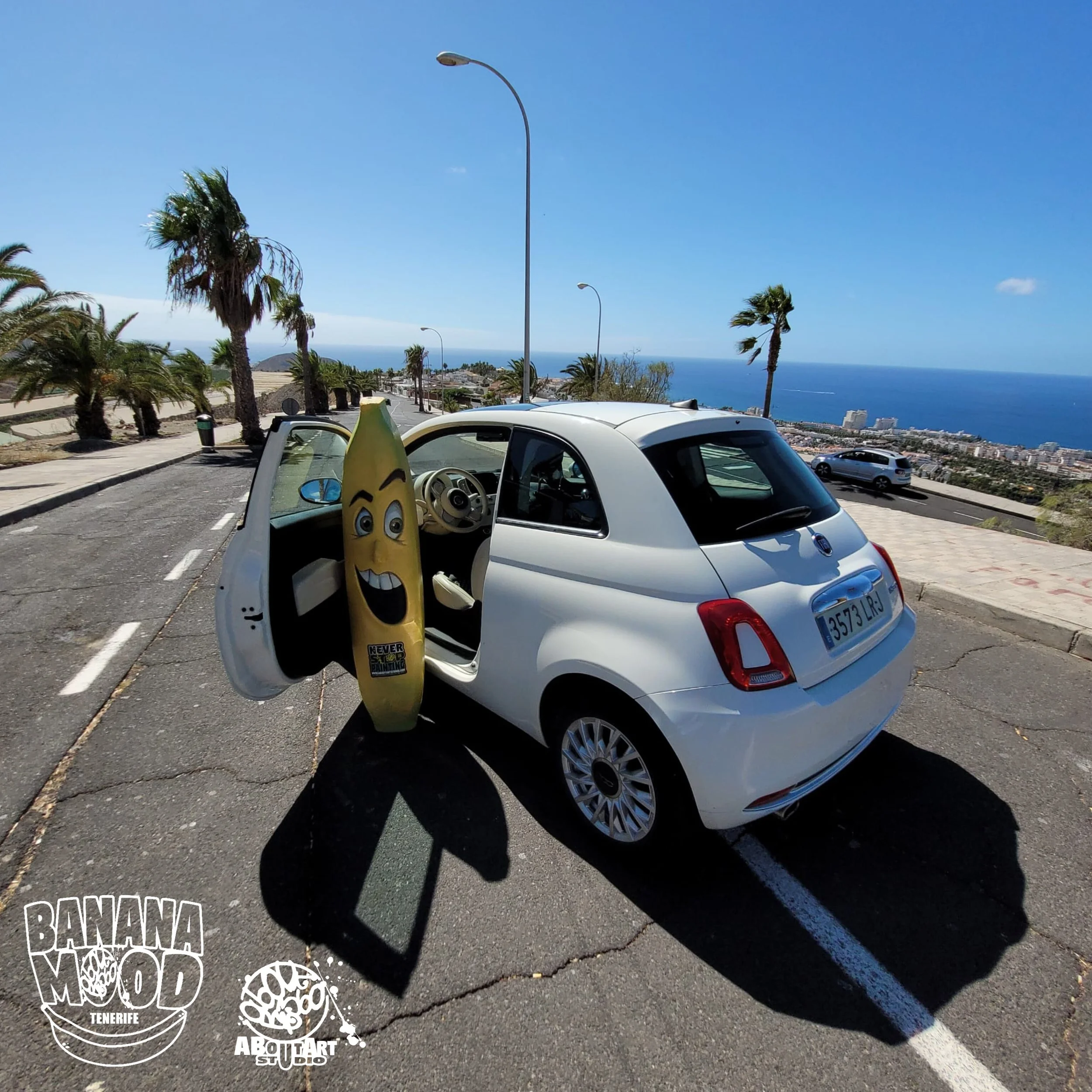Coche pequeño blanco con una banana animada en la puerta abierta y con un paisaje del mar y palmeras en el fondo.
