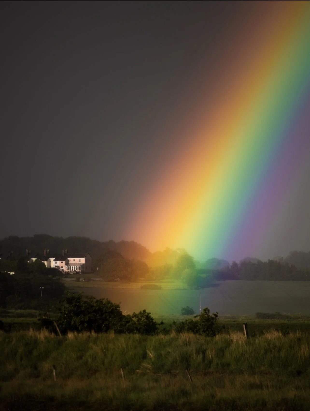 A vivid rainbow stretching from the sky over a rural landscape with houses and trees.