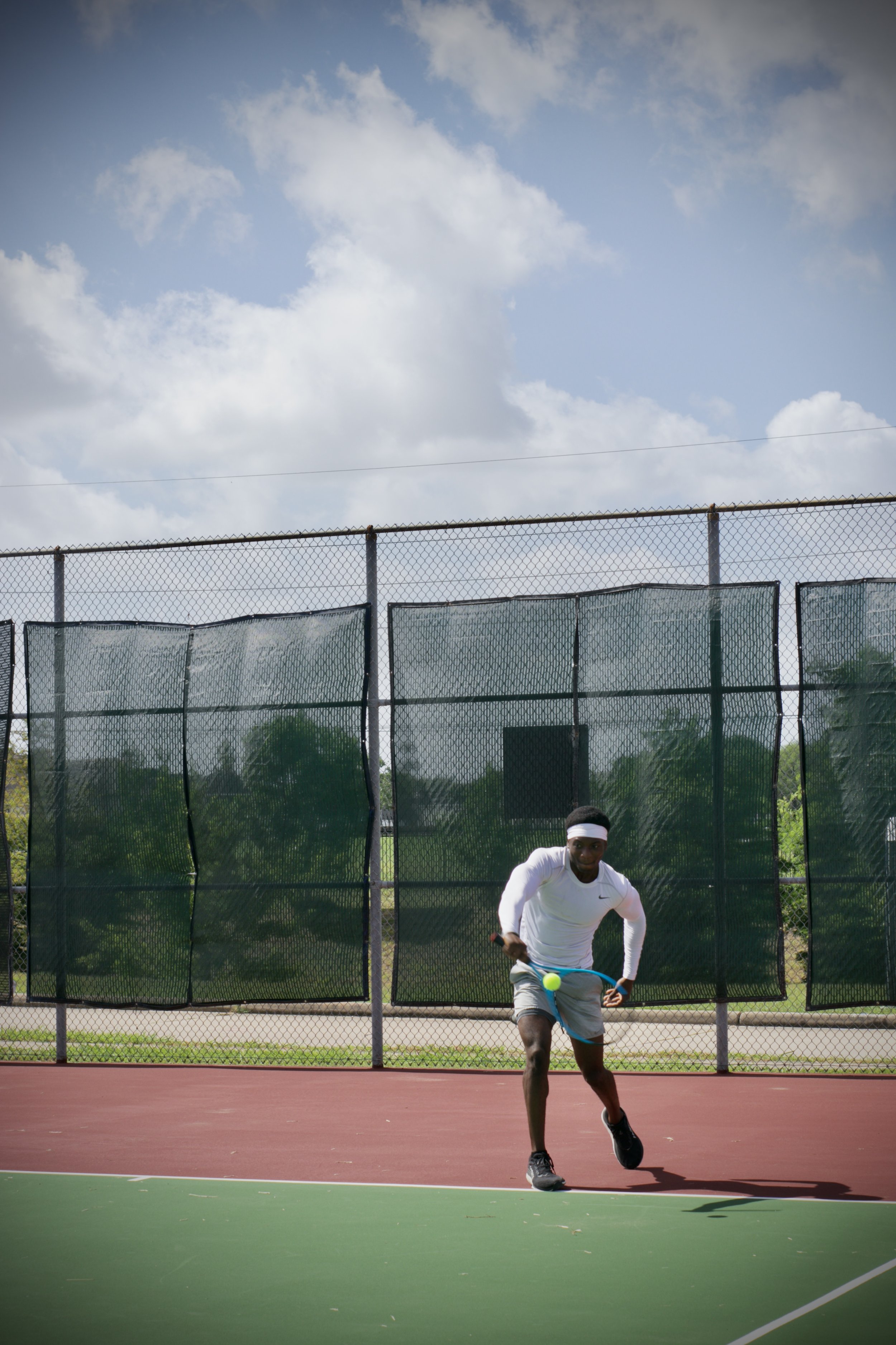 A young man in athletic attire playing tennis on an outdoor court.