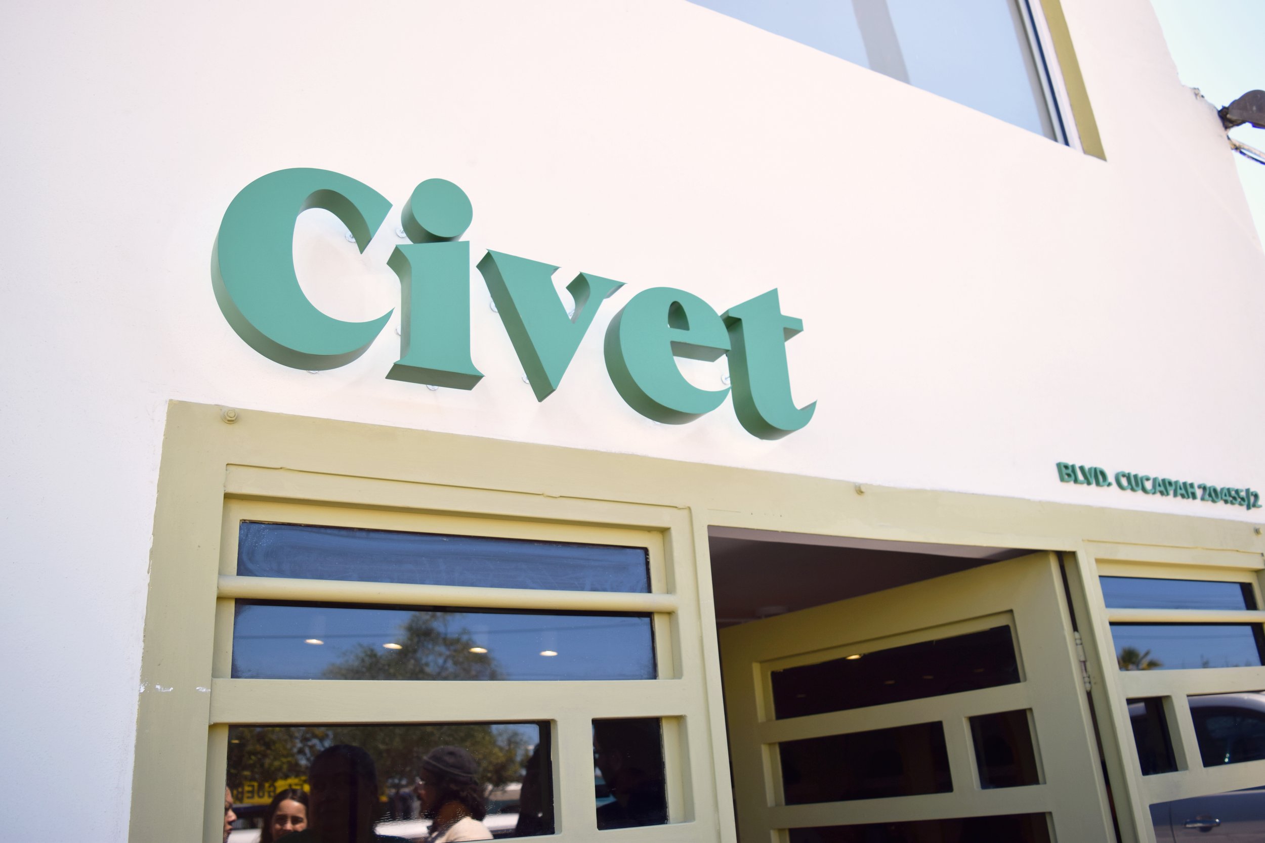 Fachada de una clínica veterinaria con el letrero 'Civet' en letras grandes y en color verde y una ventana con varias personas dentro y afuera.