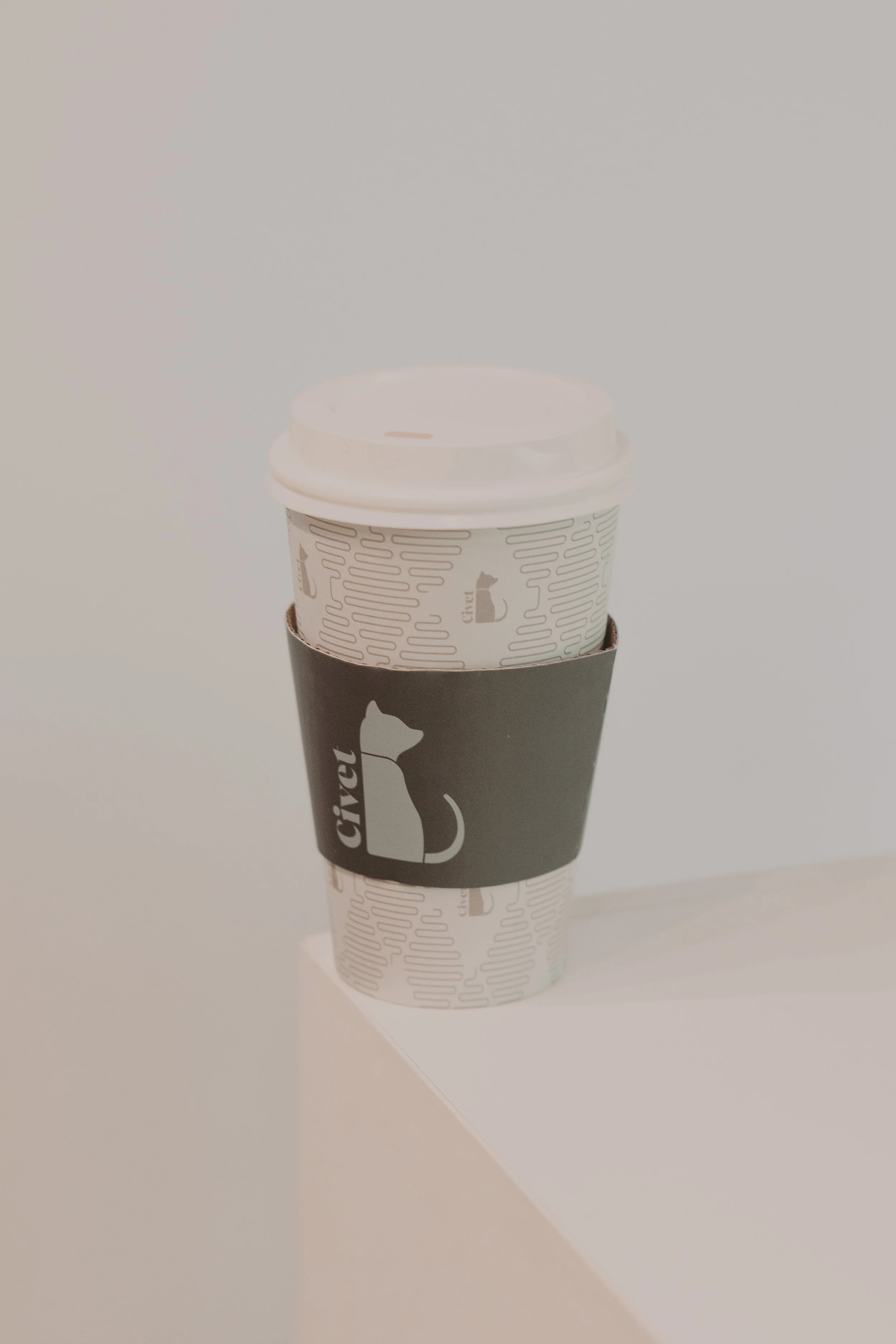 Vaso de café con tapa cubierto por un sleeve negro con logotipo de un perro gris y la palabra 'Crime' en blanco.