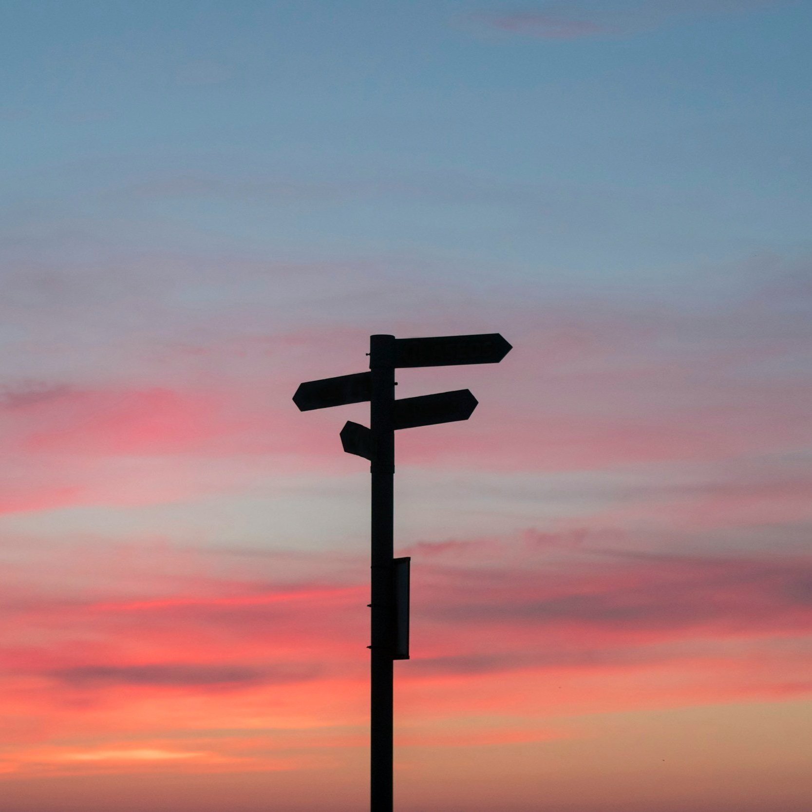 Silhouette of a multi-directional signpost against a colorful sunset sky.