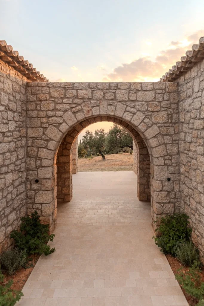 Stone archway with a tiled walkway leading to an outdoor landscape with trees at sunset.