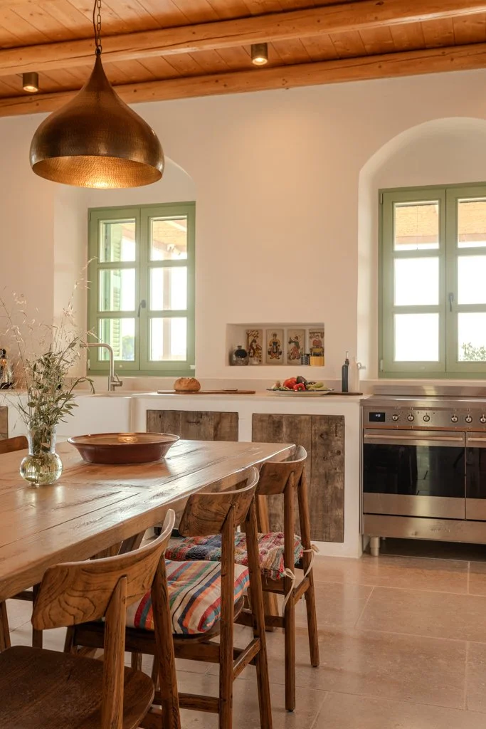 Rustic kitchen with wooden dining table and chairs, green-framed windows, a wooden ceiling, and modern appliances.
