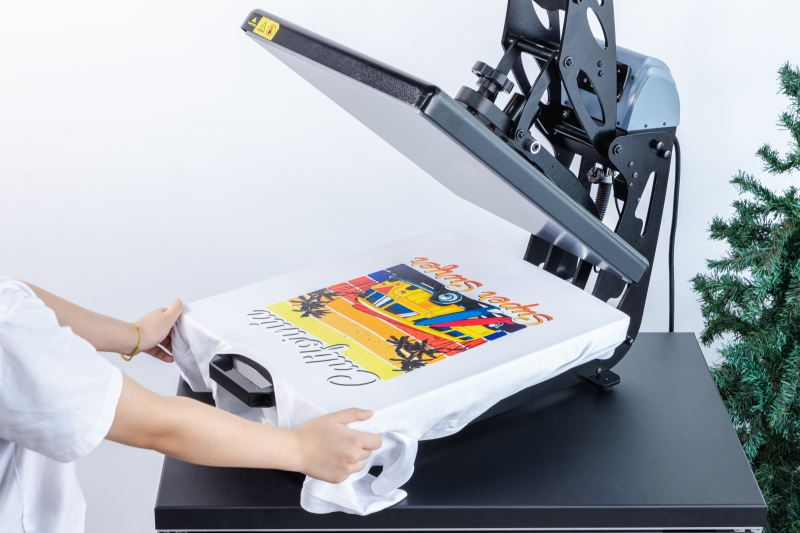 Person using a heat press machine to transfer a colorful graphic design onto a white t-shirt.