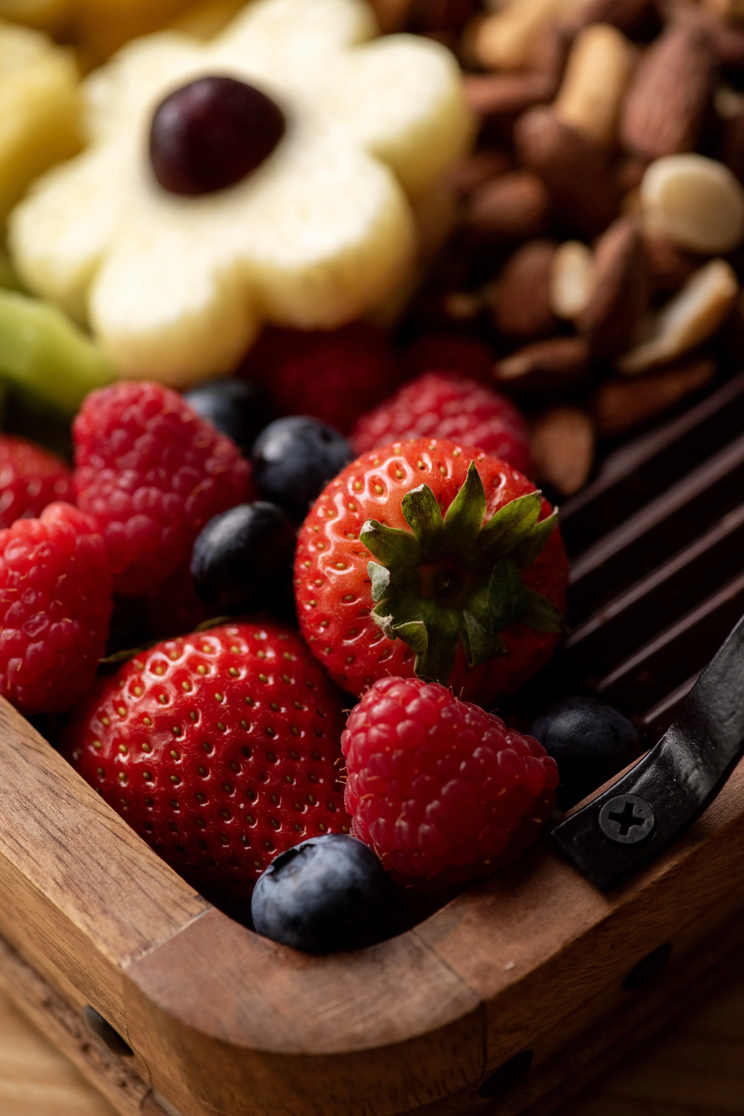 Close-up of fresh mixed berries, including strawberries, blueberries, raspberries, and blackberries in a wooden container.