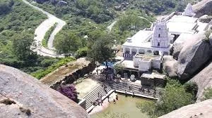 A scenic view of a mountainous area with a winding road, lush greenery, and a white building with turrets surrounded by rocks and trees.