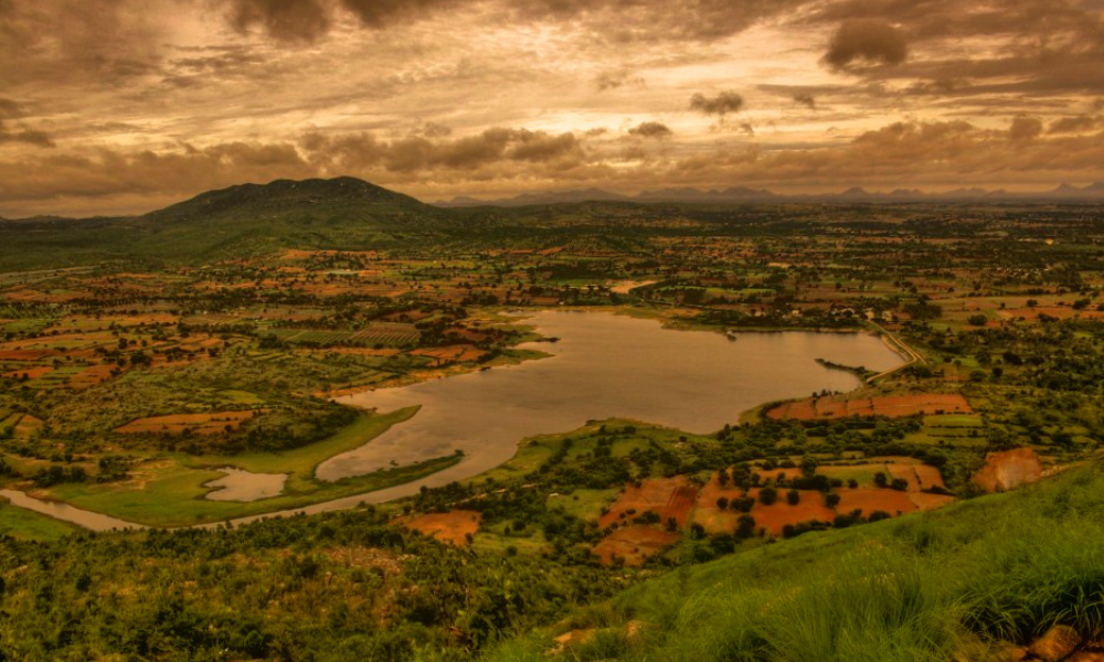 A panoramic view of a rural landscape at sunset with a river, farmland, and a mountain in the background.