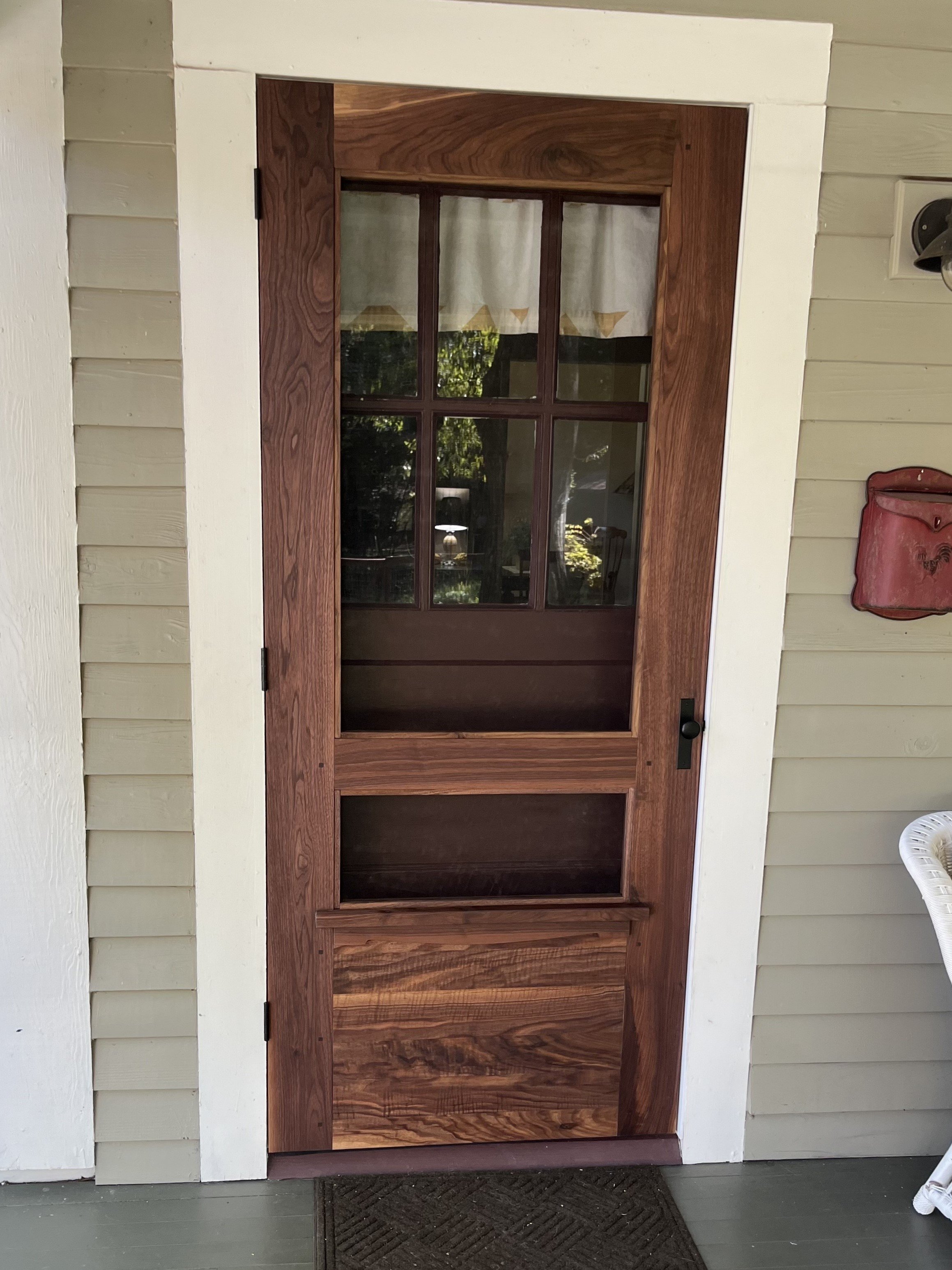 Wooden screen door with glass panes in a house with beige siding.