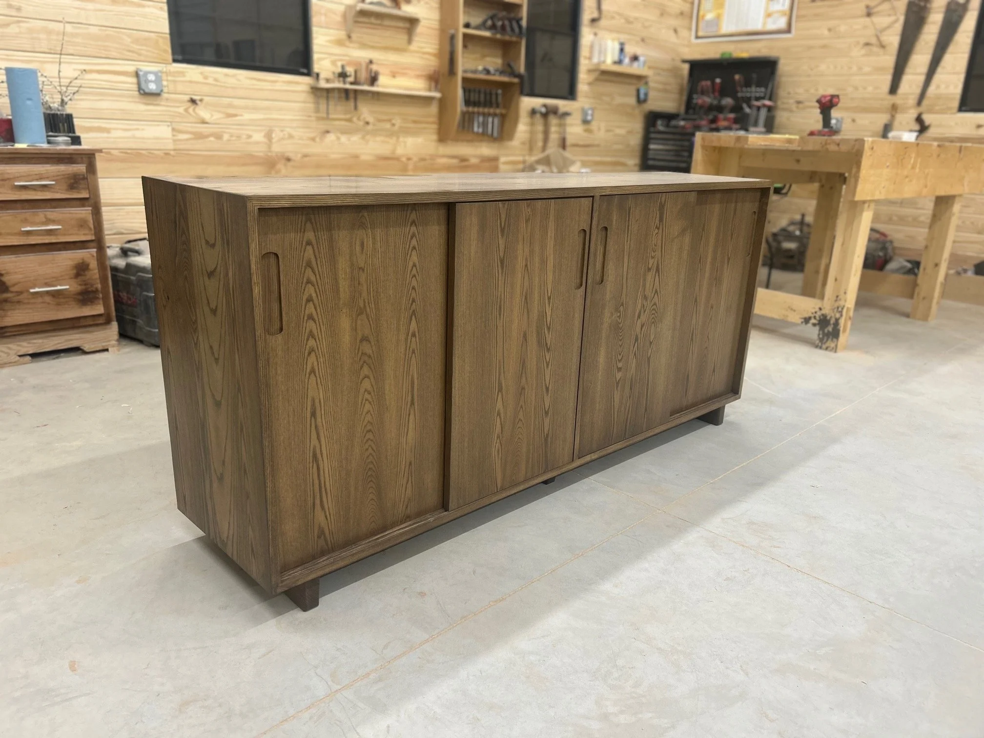 A wooden sideboard or cabinet with sliding doors in a woodworking shop.