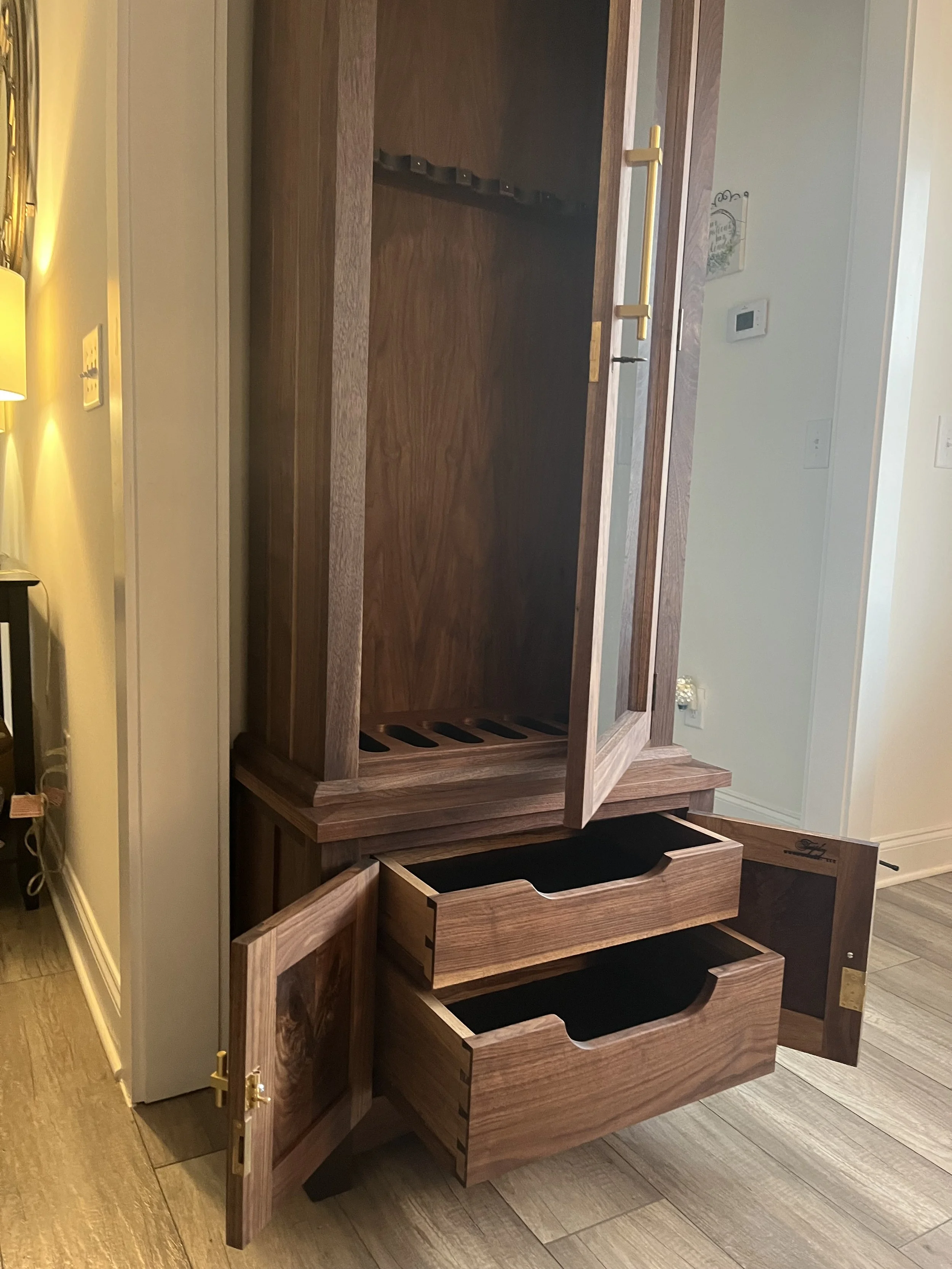 A wooden cabinet with two open drawers and two doors, showing internal compartments, placed on a wood floor in a room.