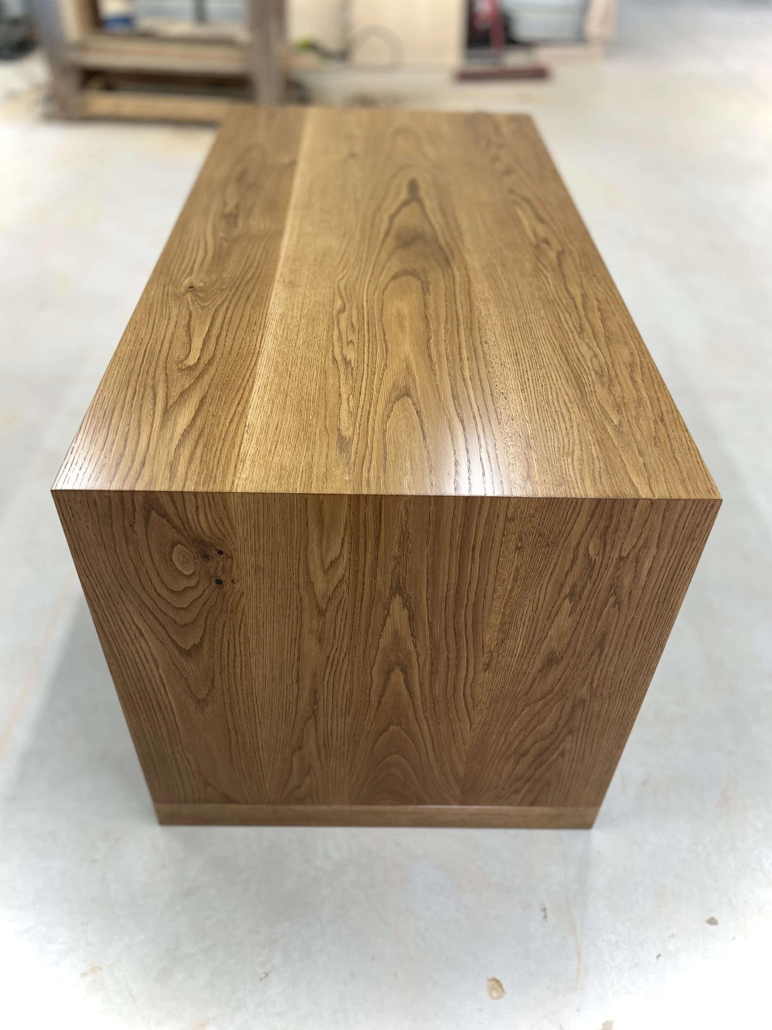 A rectangular wooden block with a natural wood grain finish, placed on a light-colored surface in a workshop or warehouse setting.