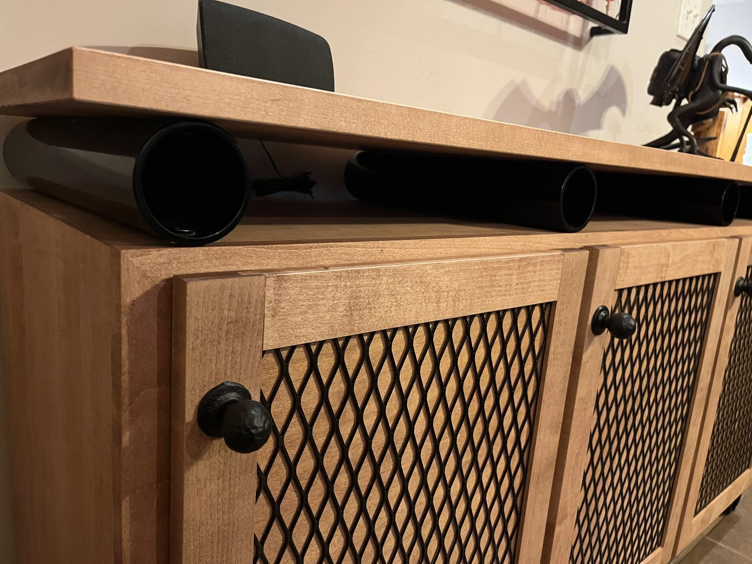 Close-up of a wooden cabinet with black mesh panels and round black handles, with a wooden tabletop on top.