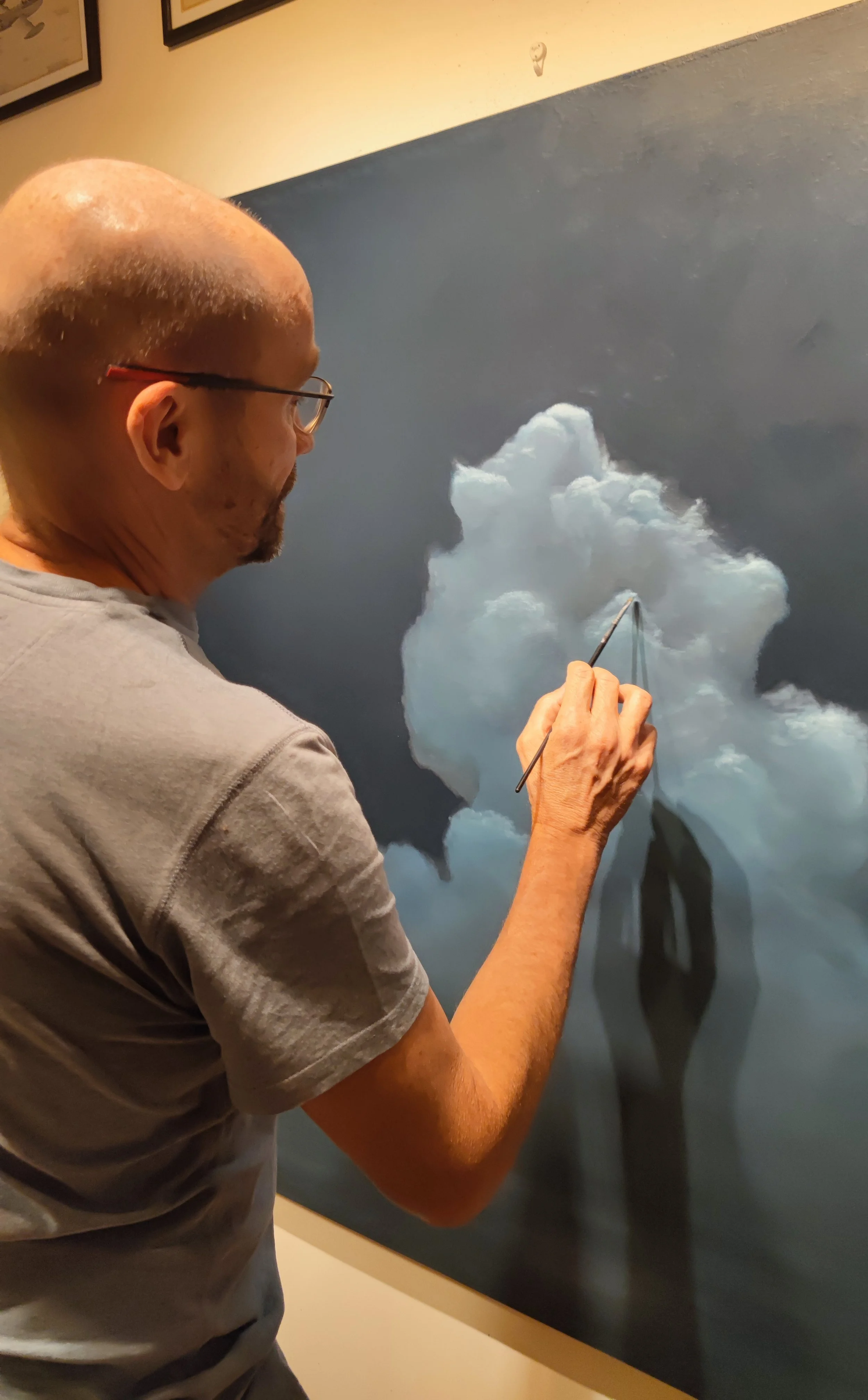 An artist painting a cloud with a small brush on a dark gray background.