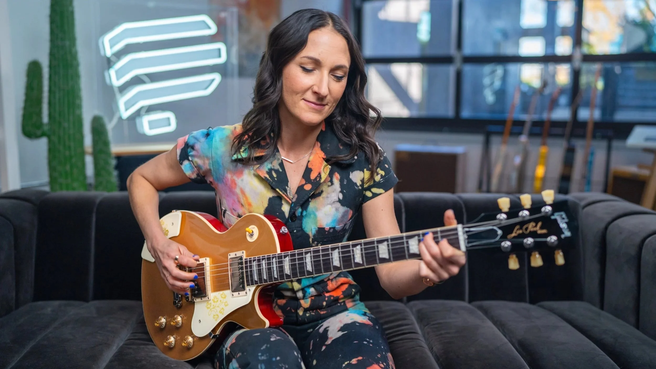Guitarist and musician Molly Miller playing a Gibson Les Paul Studio sat on a black sofa teaching for Pickup Music