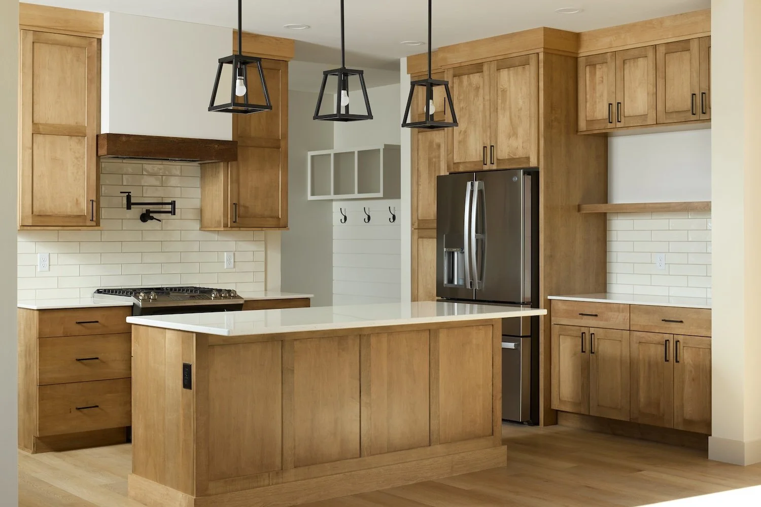 Modern kitchen with wooden cabinets, white countertops, a stove, a stainless steel refrigerator, black pendant lights, and white subway tile backsplash.