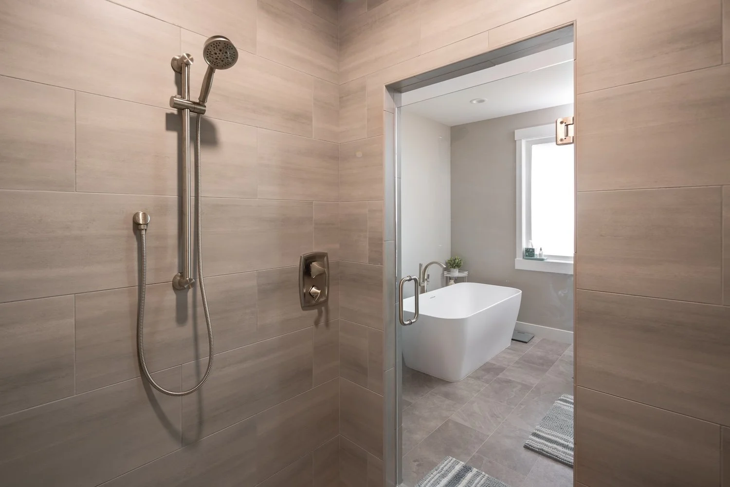 Modern bathroom with a walk-in shower area featuring a wall-mounted showerhead and a separate tub area with a window and a small potted plant.