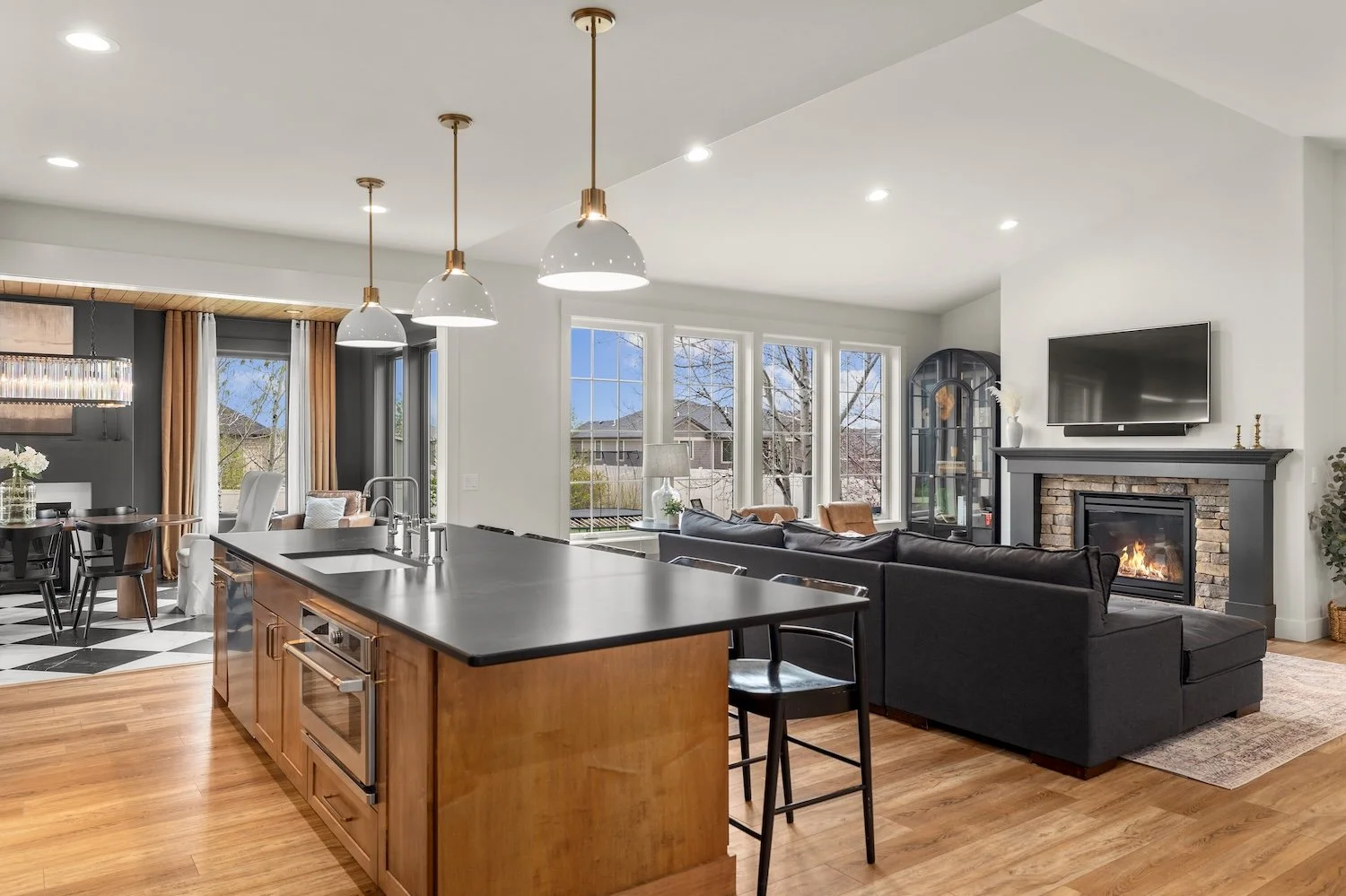 Open-concept living room and kitchen with hardwood floors, a fireplace, a mounted TV, large windows, and modern decor.