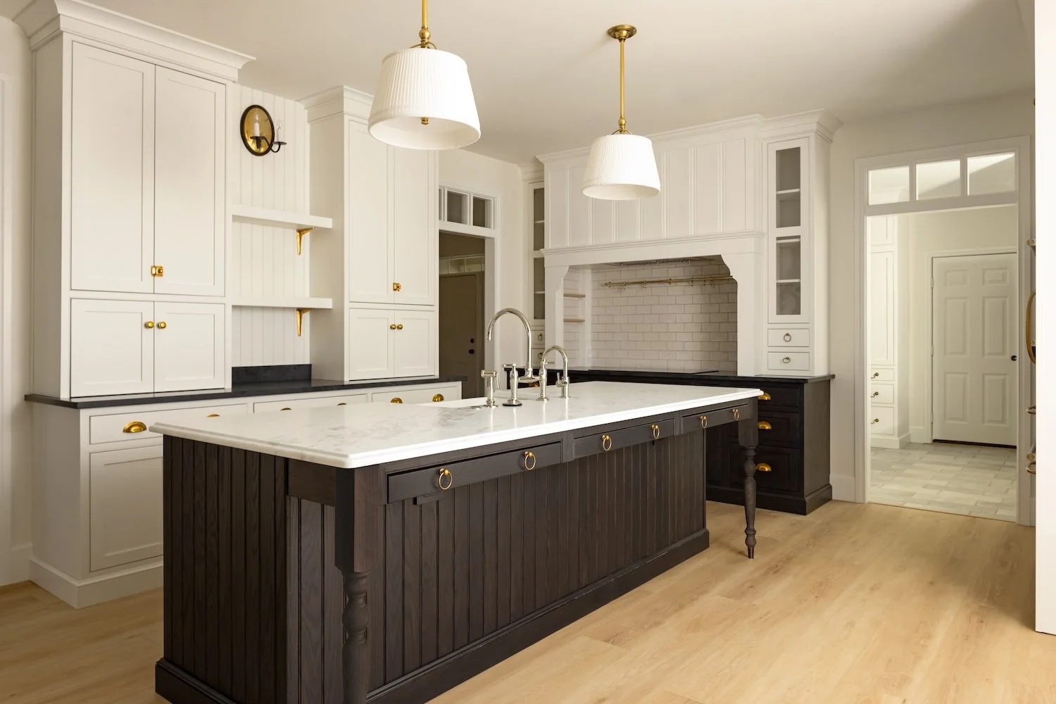 Modern kitchen with white cabinets, black countertops, and a dark wood island with a marble top, pendant lights, and brass accents.