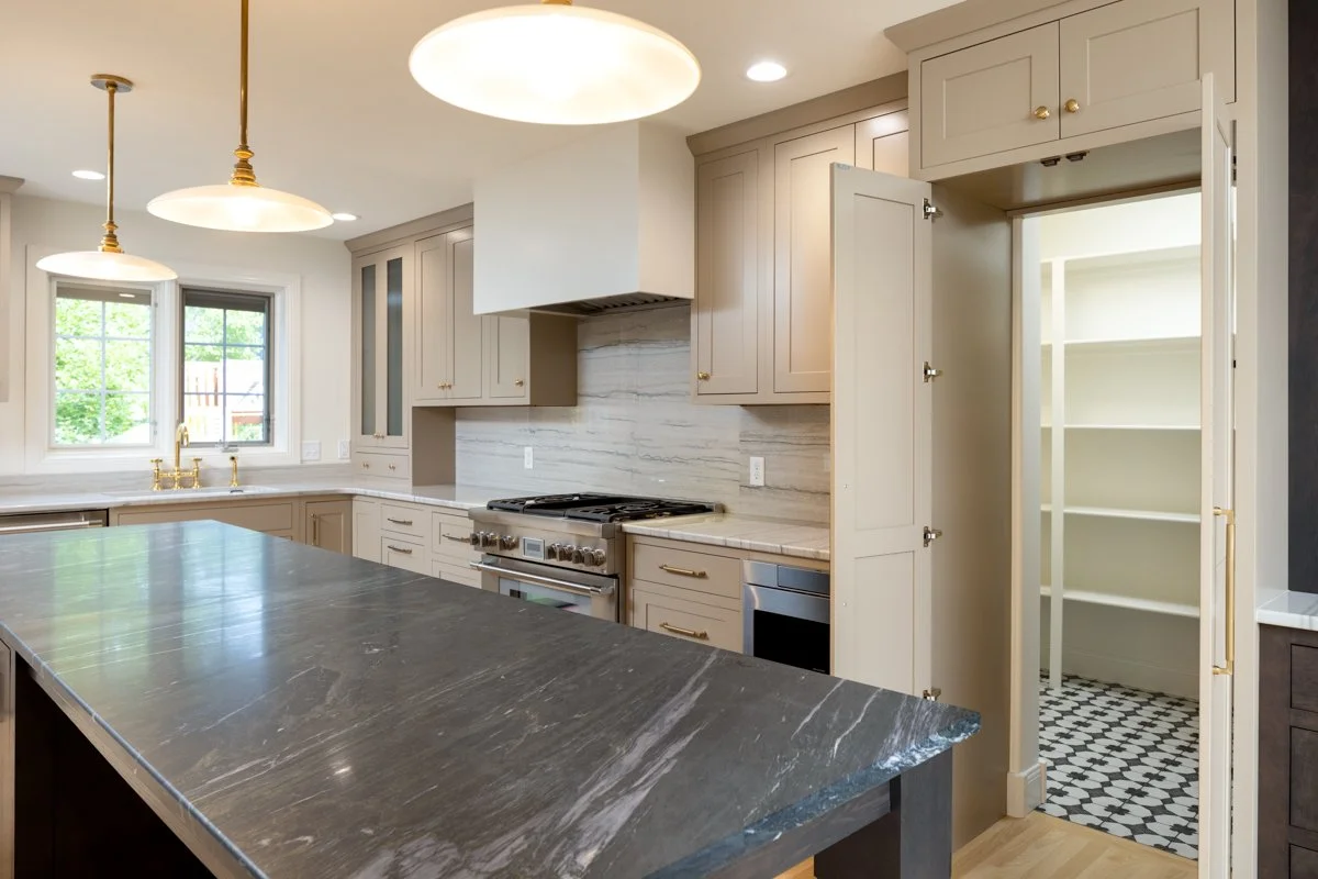 Modern kitchen with beige cabinets, black and white patterned pantry, and marble countertops.