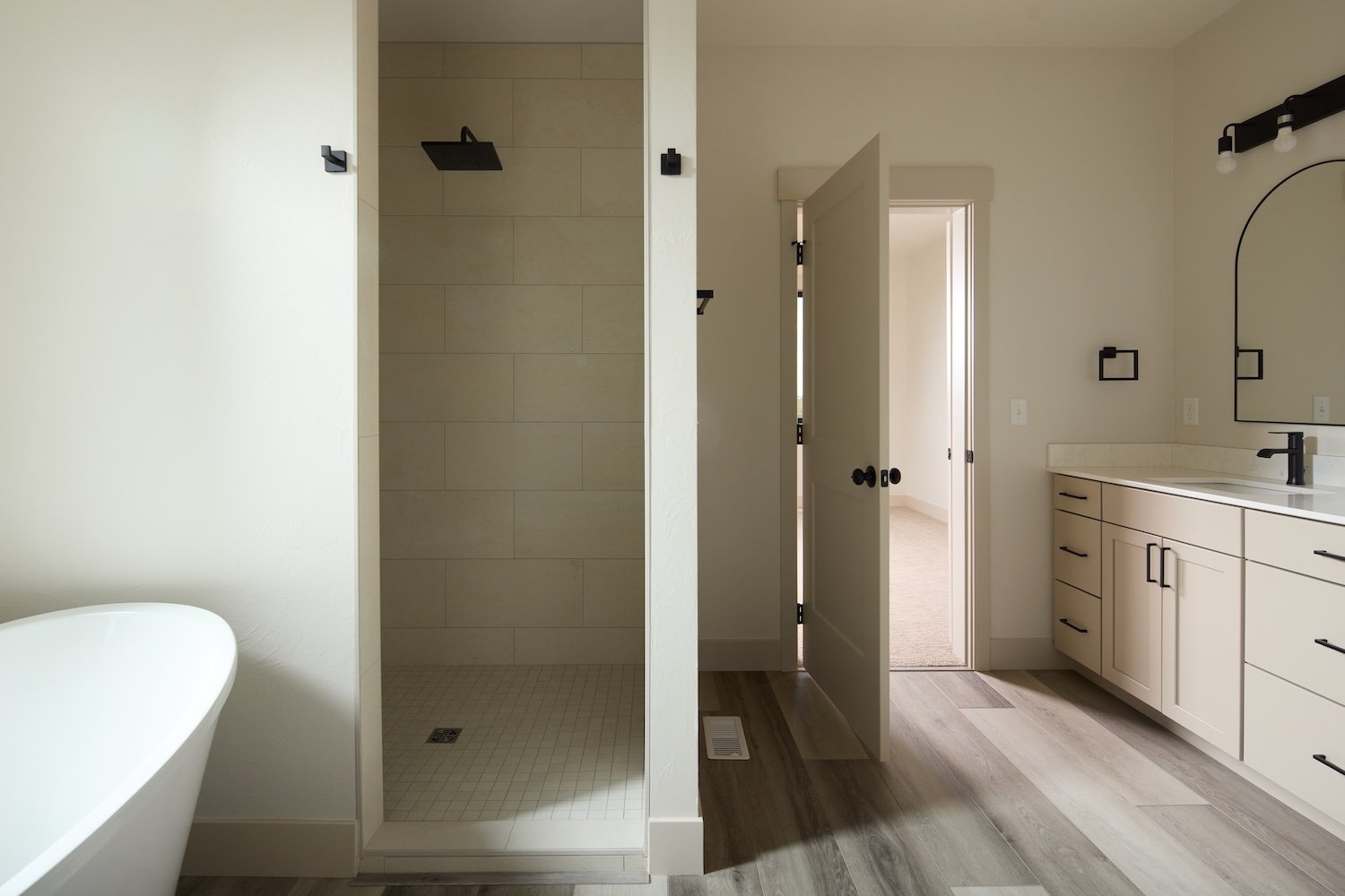 Modern bathroom with walk-in shower, bathtub, white vanity with black hardware, and a large mirror.