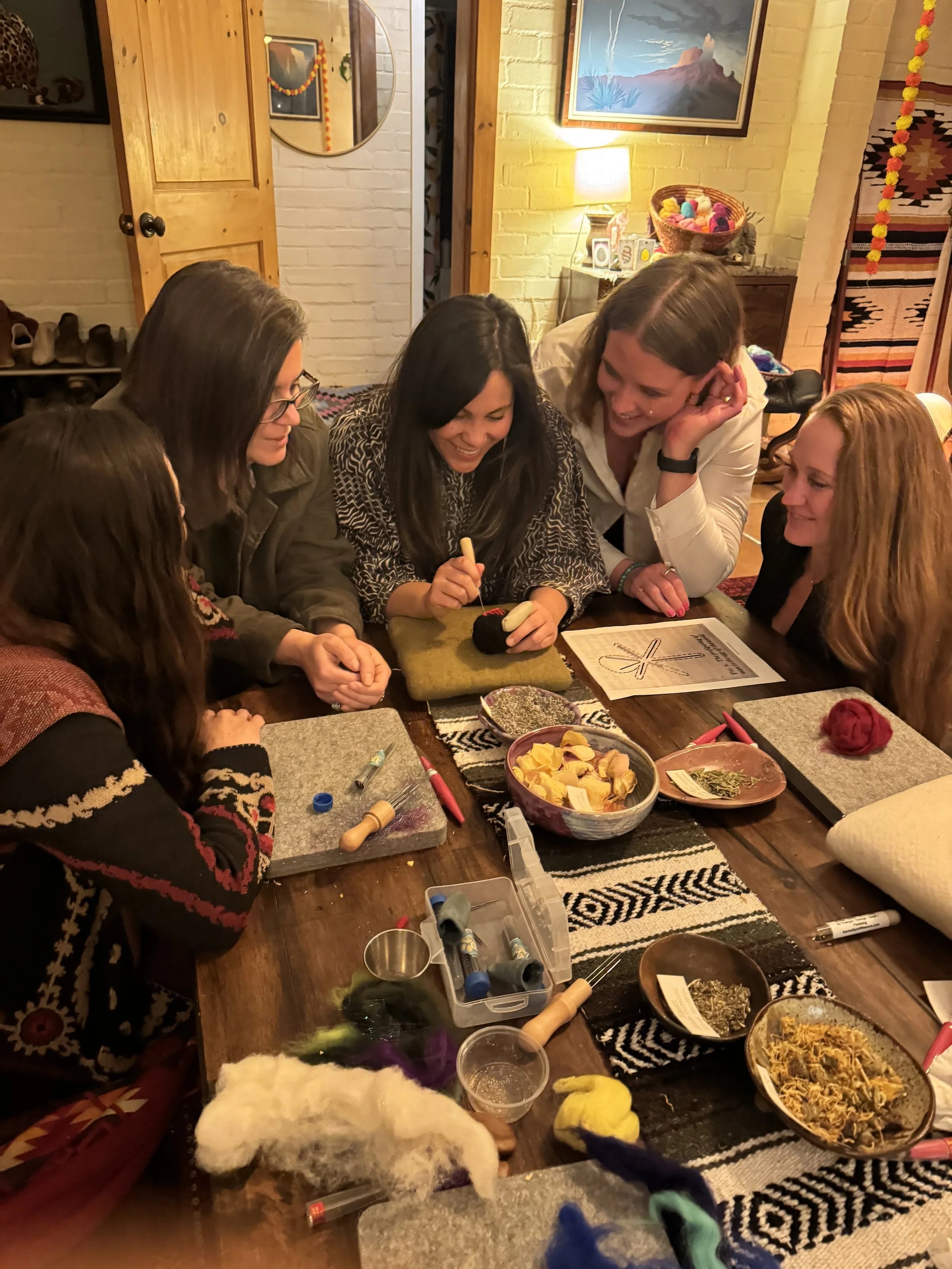 Group of women gathered around a table, engaged in a craft activity with various supplies and materials on the table.