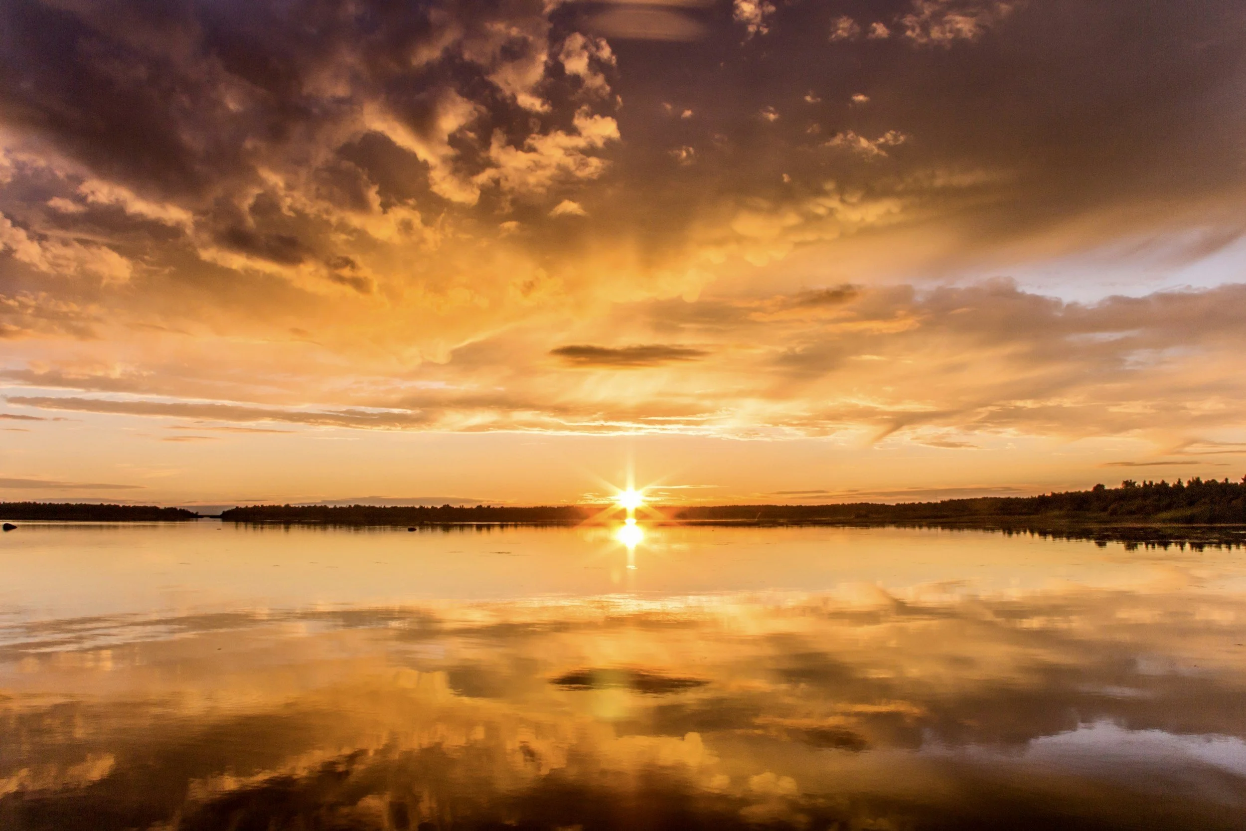 Sunset over a calm river with vibrant orange and purple clouds reflected in the water.