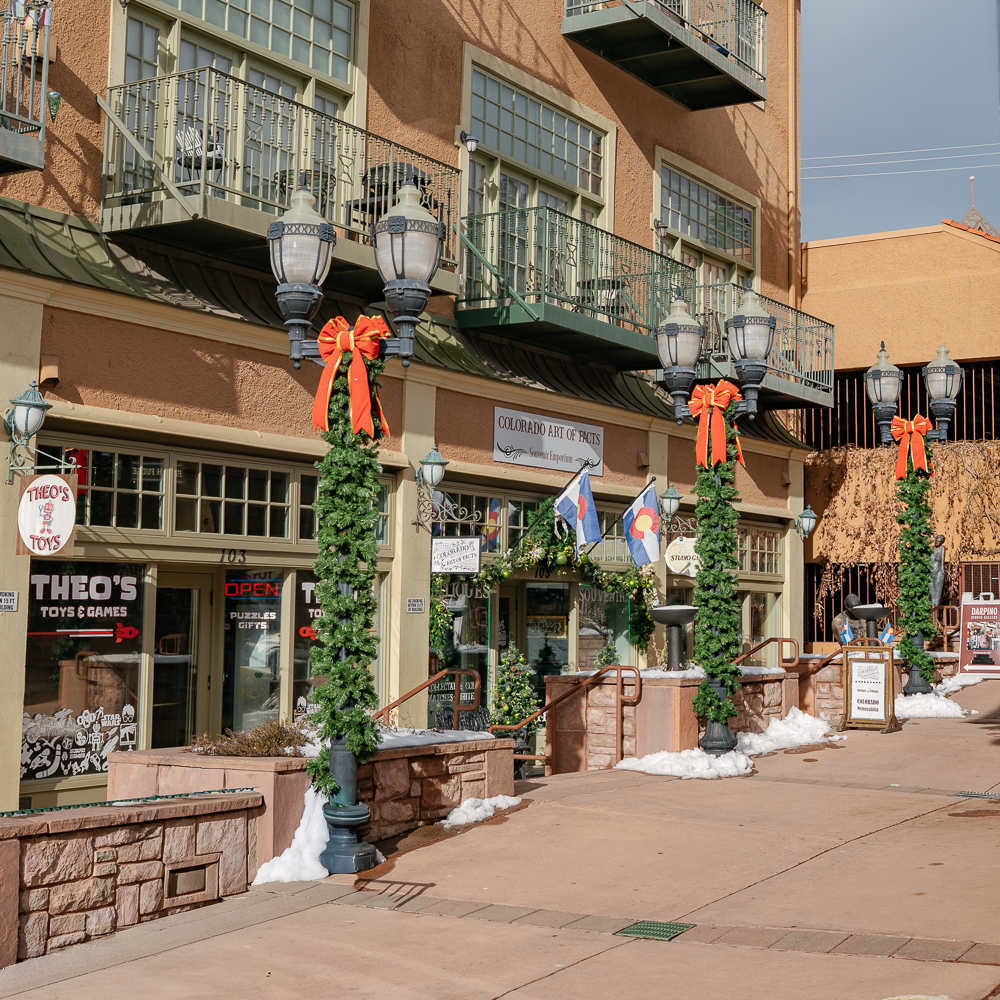 Holiday-themed commercial photo of Manitou Springs shops, featuring decorated lamp posts, local boutiques, and downtown architecture.