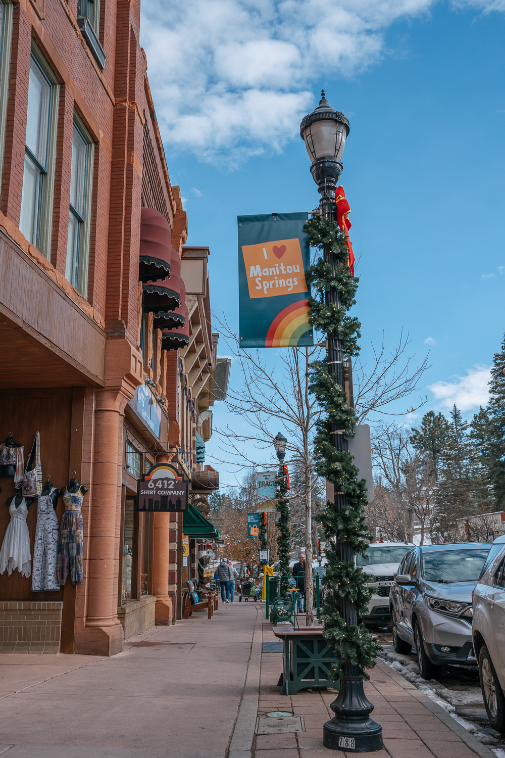 Commercial street photography of downtown Manitou Springs featuring local shops, holiday garland, and the ‘I Love Manitou Springs’ banner.