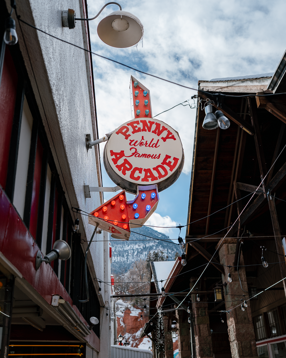 Manitou Springs Penny Arcade sign with colorful lights and mountain views in the background, captured as part of downtown commercial branding.