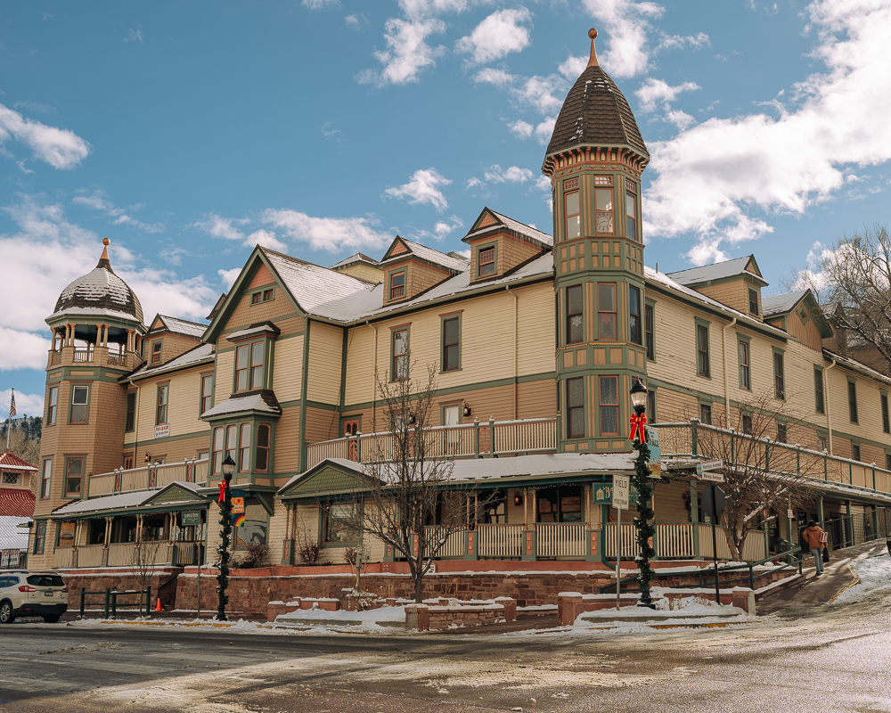 Winter photo of The Barker House in Manitou Springs, showcasing its historic Victorian architecture, snow-covered exterior, and holiday décor against a bright Colorado sky.