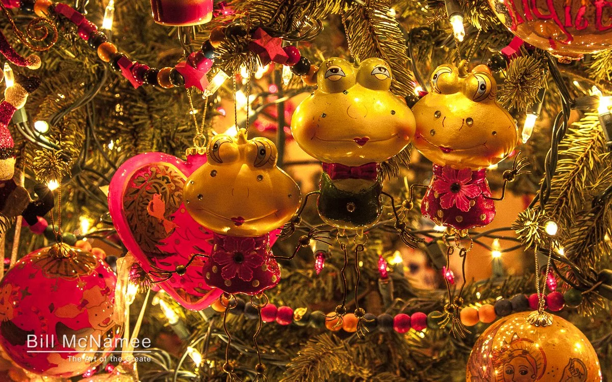 Playful frog ornaments hanging together on a Christmas tree with warm holiday lights and decorative garland.