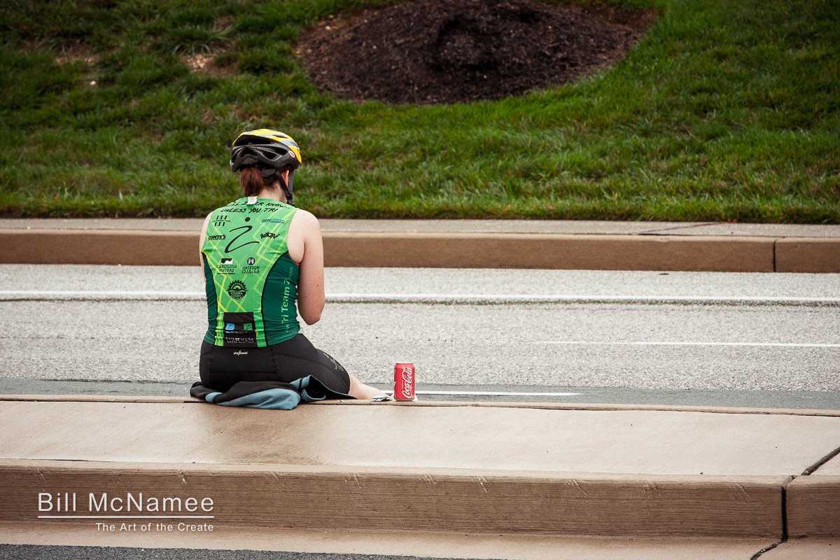 Cyclist sitting on a wet curb during 24 Hours of Booty in Columbia, Maryland, with a red Coca-Cola can beside her.