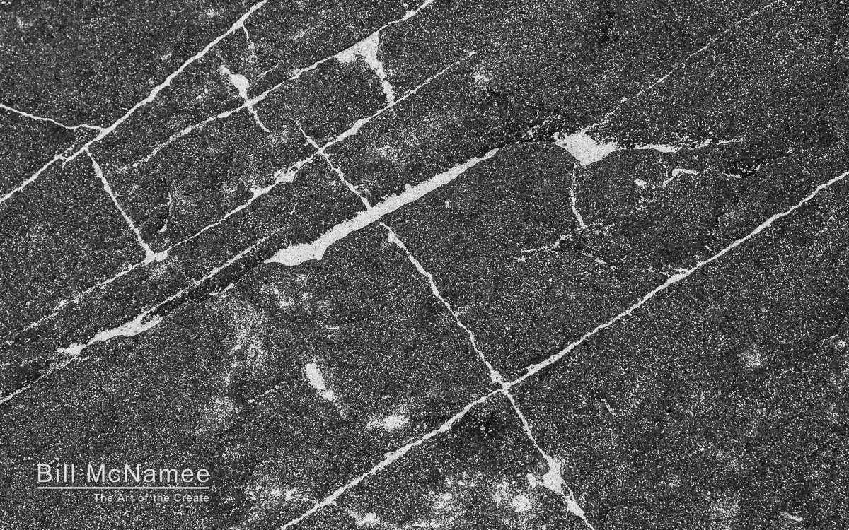 Black-and-white close-up of a Cape May jetty rock with pale sand tracing intersecting cracks across its textured surface.
