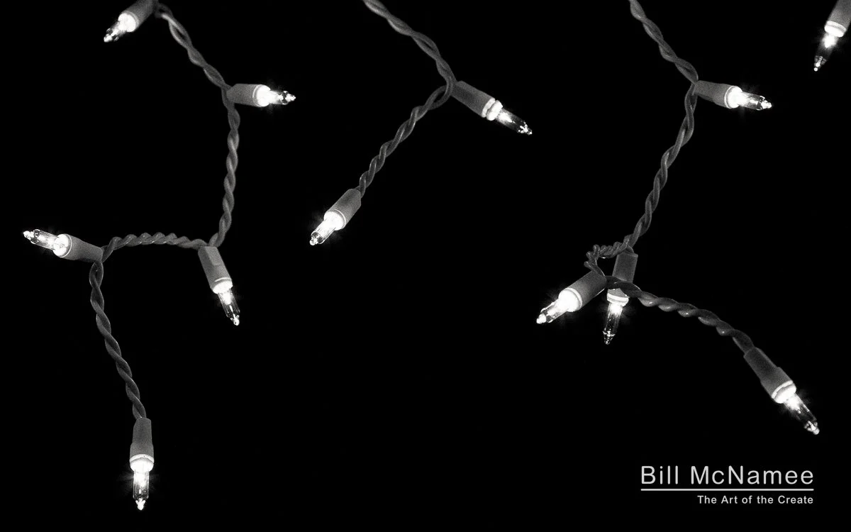 Close-up black and white photo of incandescent icicle lights glowing against the night.