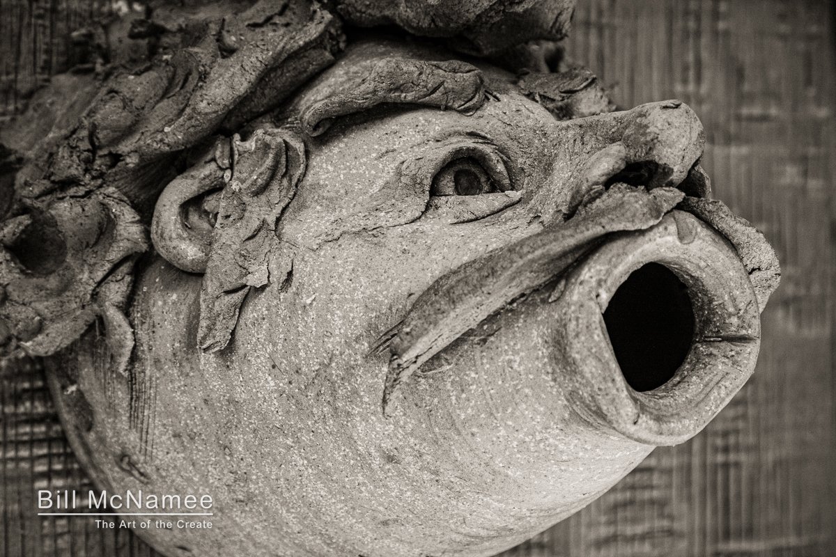 Clay birdhouse shaped like a face mounted on a barn wall, showing rough texture, circular opening, and weathered detail.
