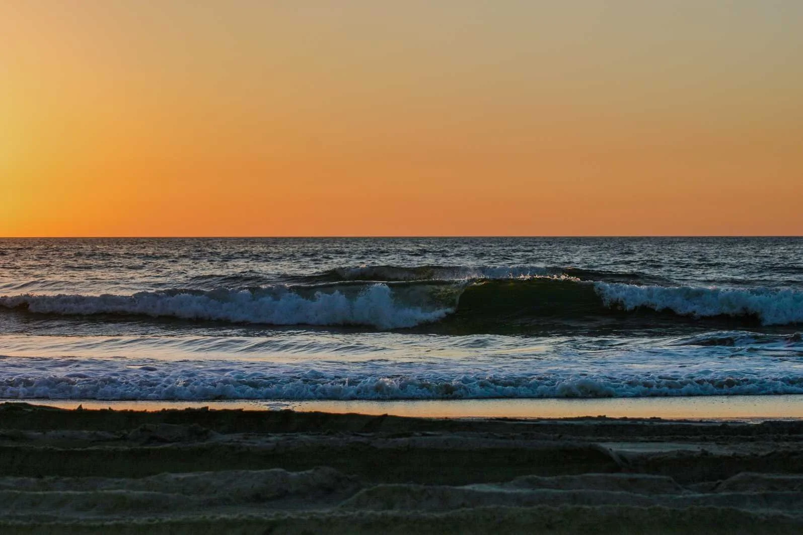 Sunset over the ocean with waves breaking on the sandy beach.