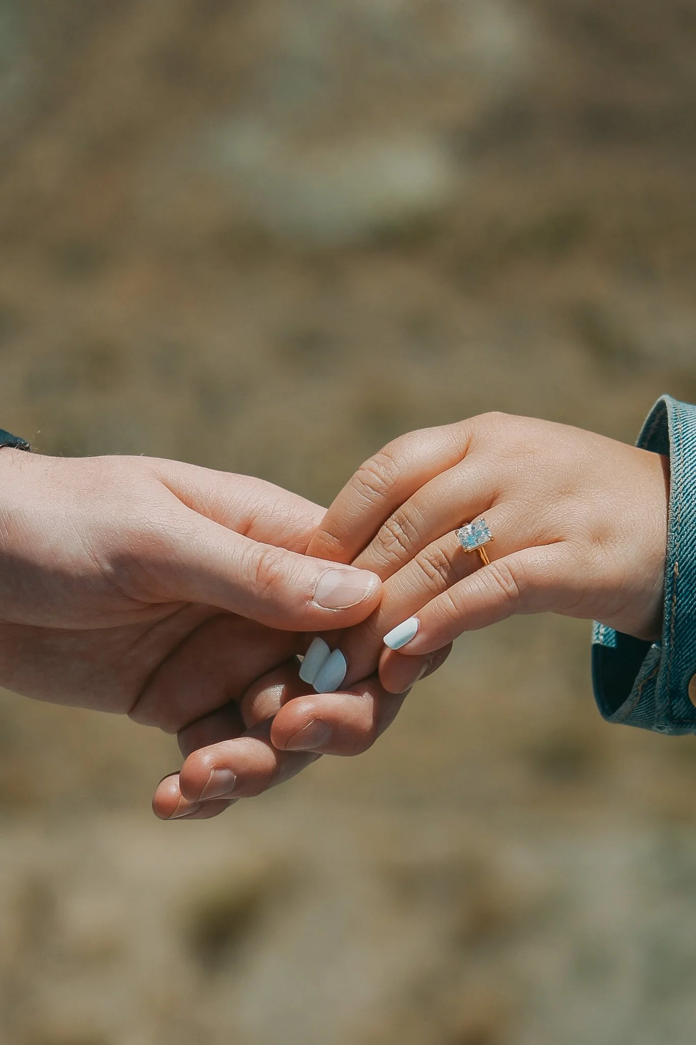 Close-up of a couple holding hands, with a focus on a ring with a large gemstone on the woman's finger.