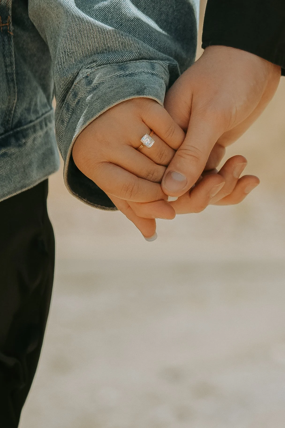 Close-up of two hands holding each other, with one person wearing a ring and denim jacket.