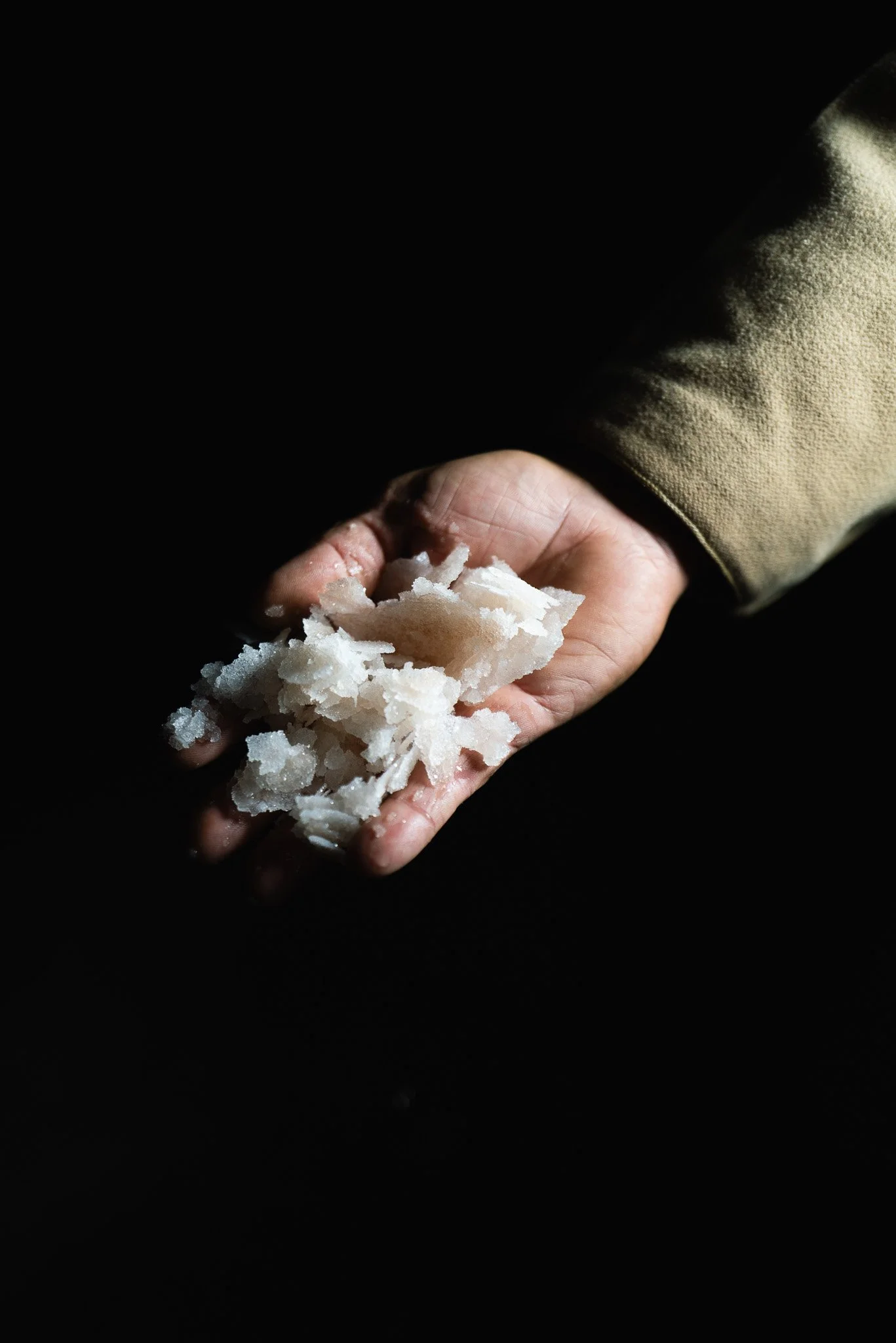 Eine Hand hält grobes Salz gegen einen dunklen Hintergrund.