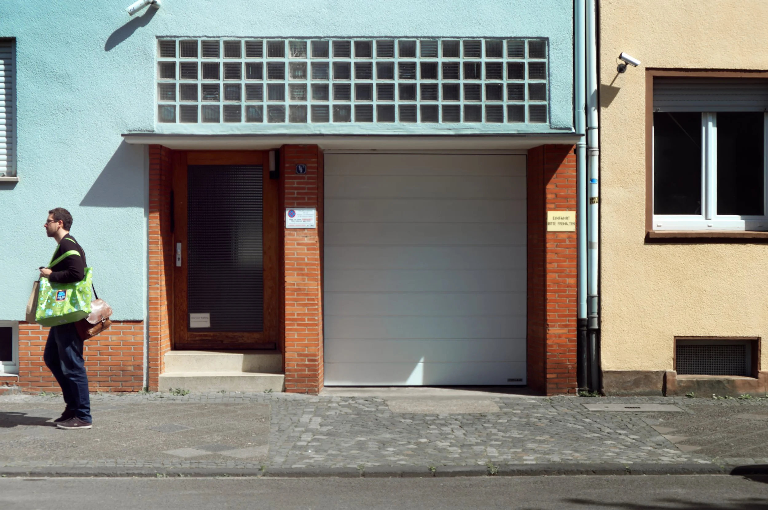 Ein Mann läuft auf der Straße vorbei an einem zweifarbigen Haus mit blauer und gelber Fassade, einem Fenster und einer Garage.