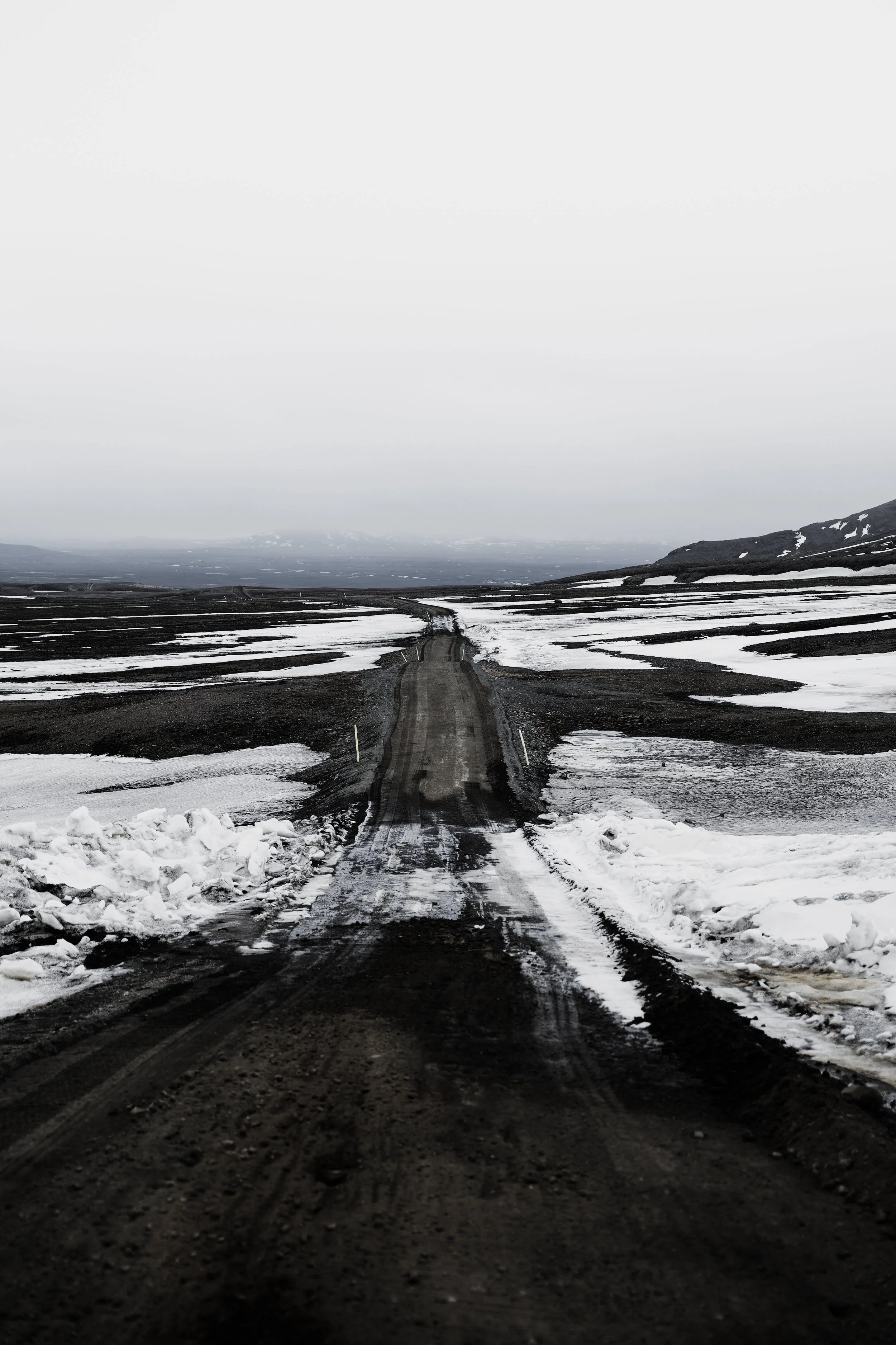 Eine abgelegene, unbefestigte Straße in einer winterlichen, schneebedeckten Landschaft mit dunklem Himmel.