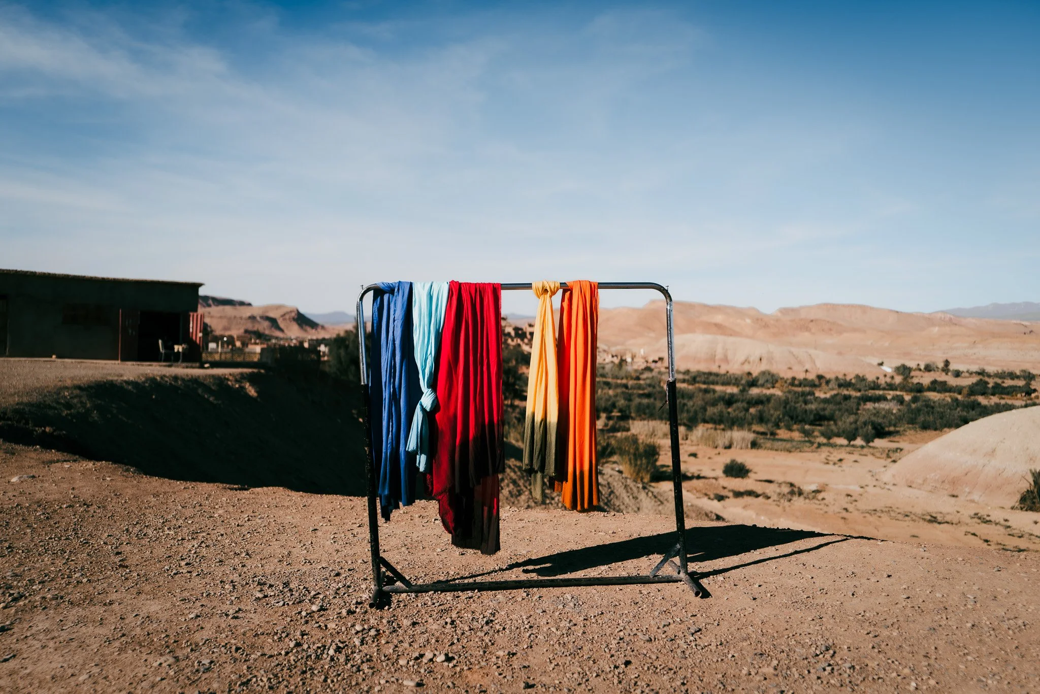 Bunte Kleidung hängt an einem Wäschekorb in einer Wüstenlandschaft mit Bergen im Hintergrund.