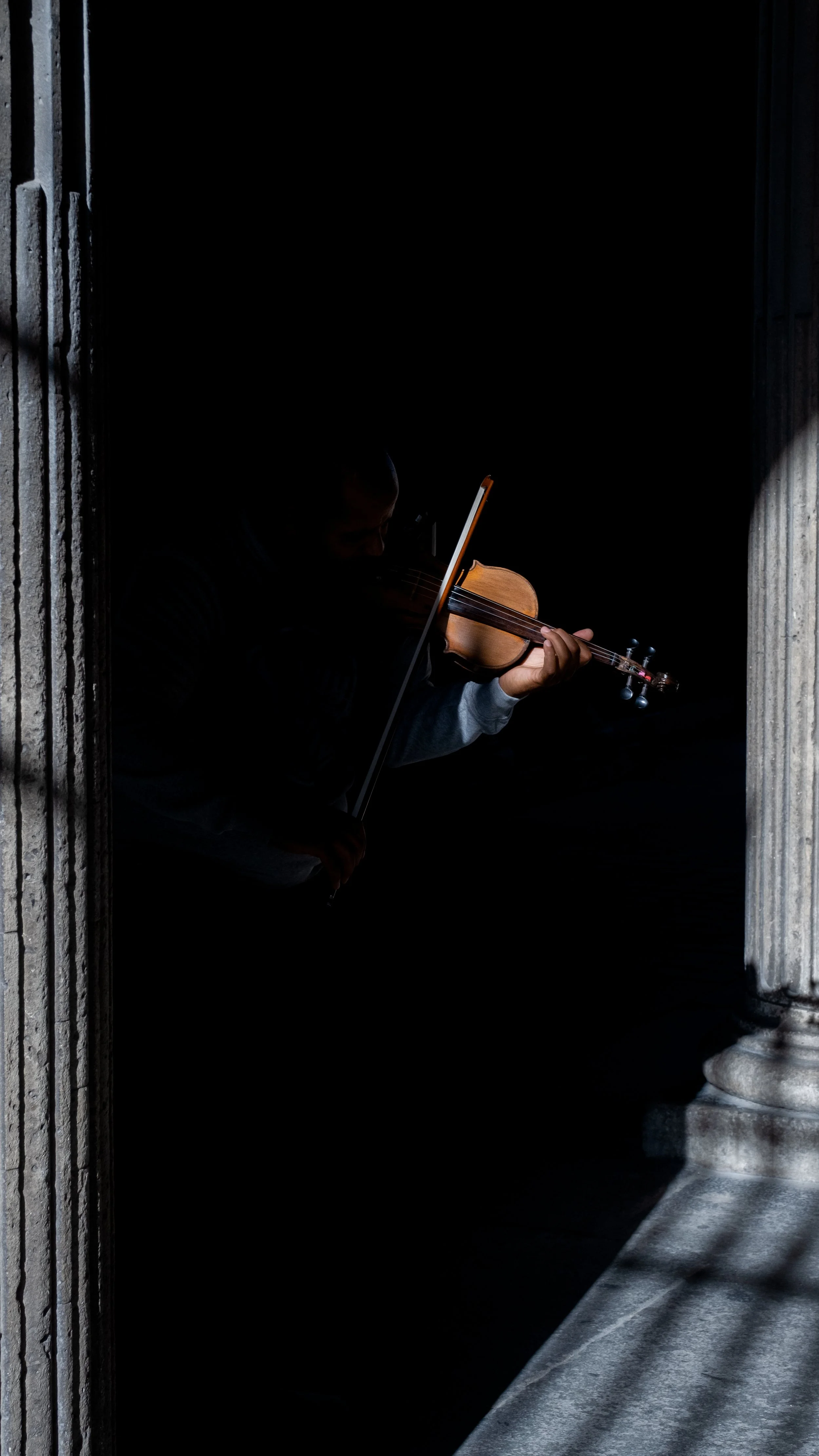 Ein Musiker spielt Violine in einem dunklen Ambiente, sichtbar nur durch das Licht auf dem Instrument und der Hand des Spielers.