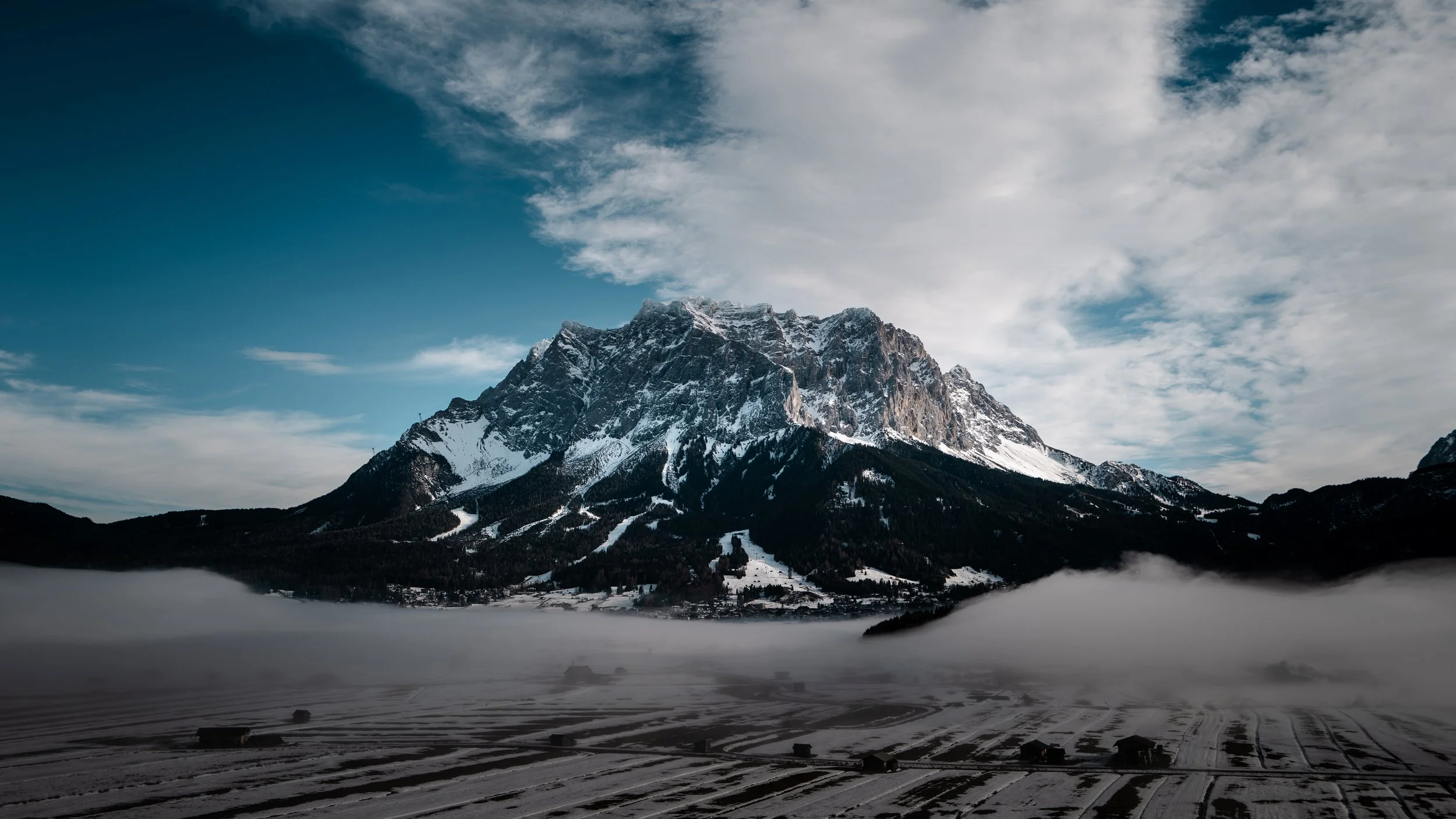 Schneebedeckte Berge mit Wald und Nebel im Tal, blauer Himmel mit Wolken